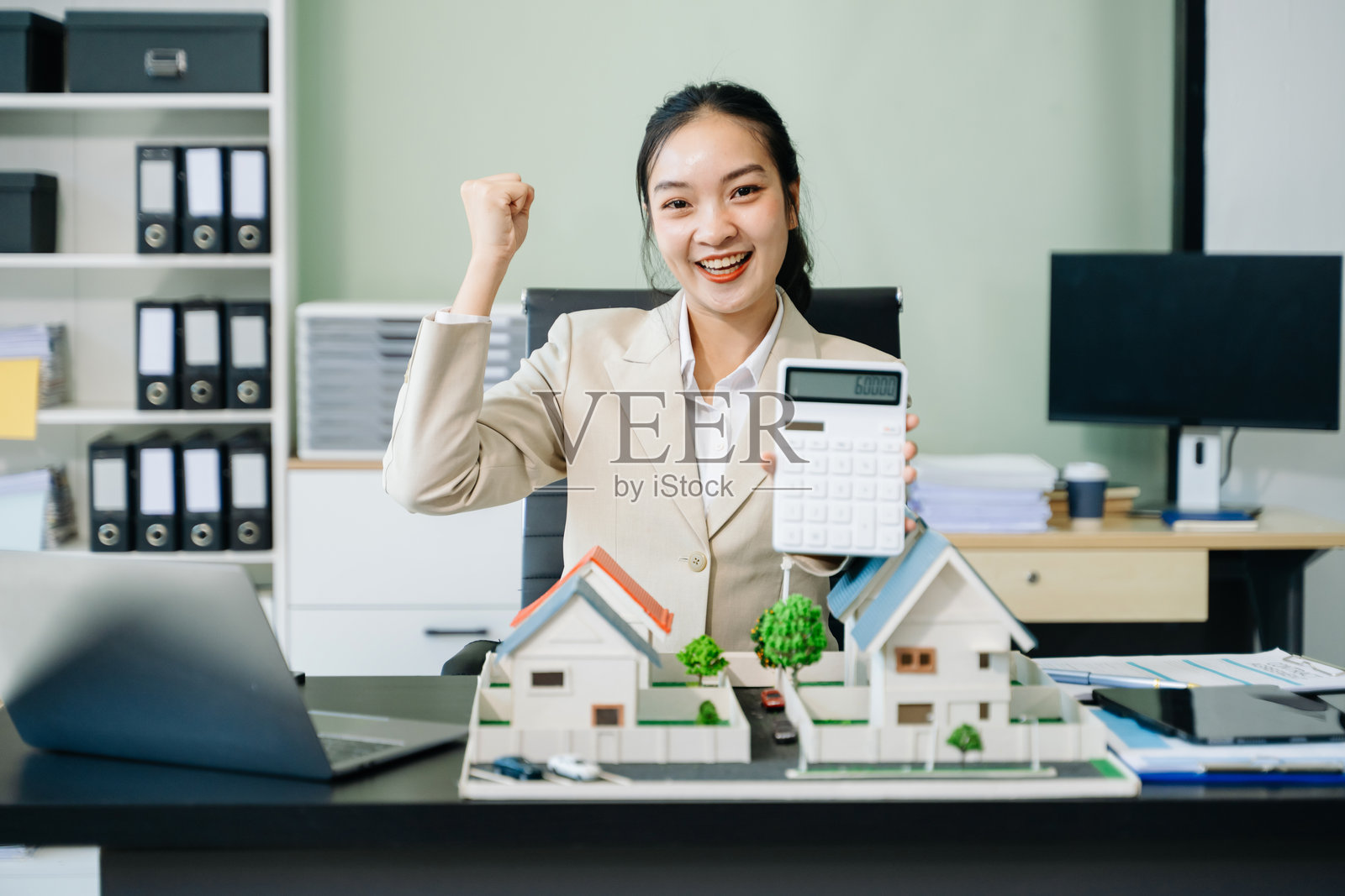 年轻的房地产经纪人，在桌边使用笔记本电脑和平板电脑工作，旁边放着一个小房子。照片摄影图片