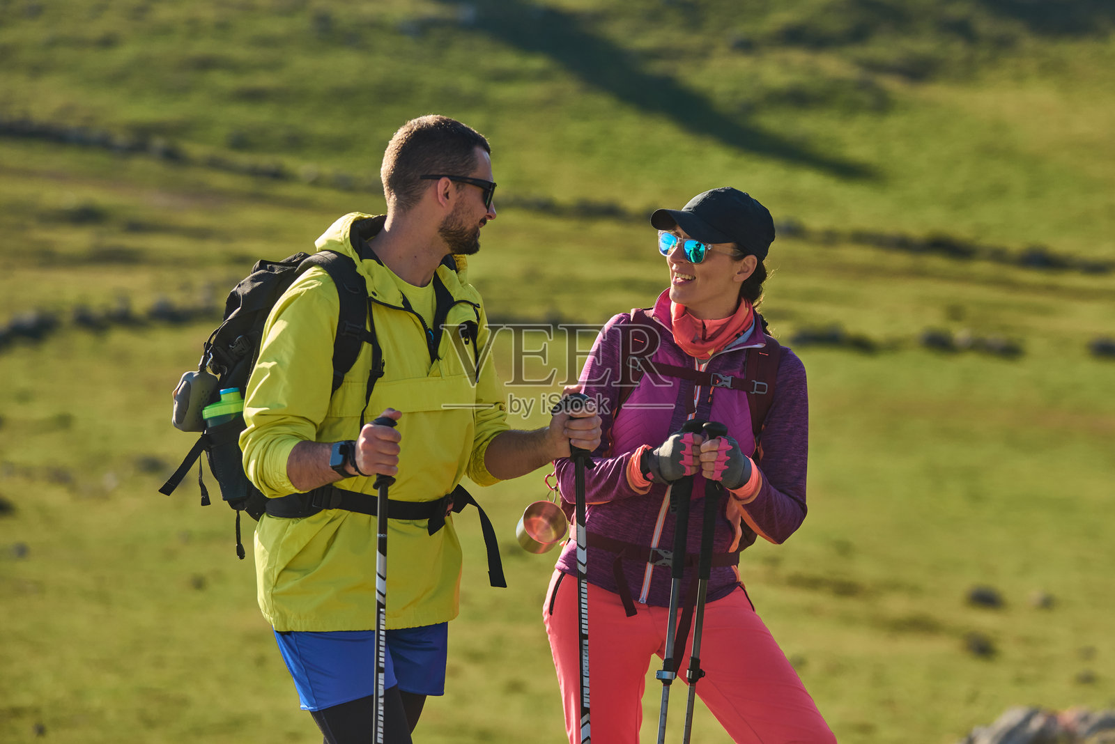 一对情侣在阳光明媚的日子里，手持登山杖，在郁郁葱葱的绿色景观中一同徒步旅行照片摄影图片