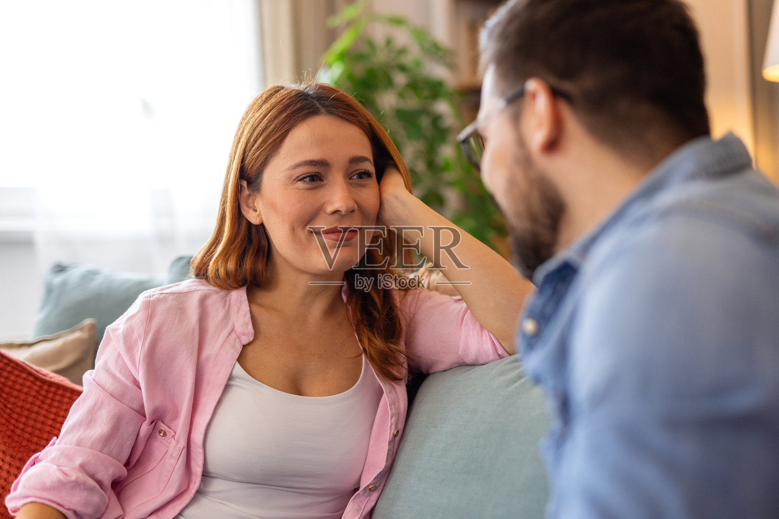 家里的沙发上，年轻美丽的女子深情地望着伴侣。幸福的情侣在舒适的客厅里交谈，共度时光。照片摄影图片