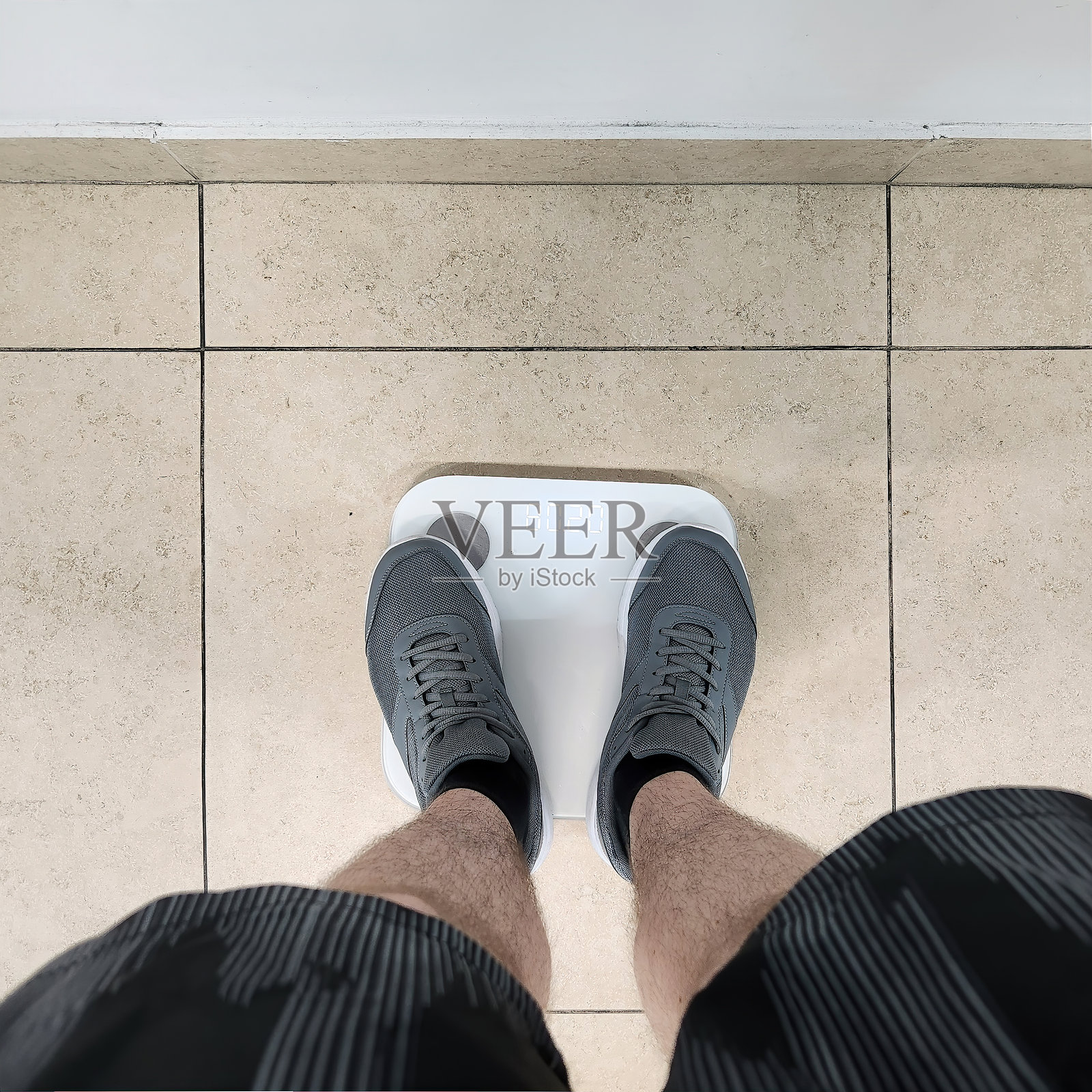 一个穿着运动短裤和运动鞋的男人正在电子体重秤上称重照片摄影图片