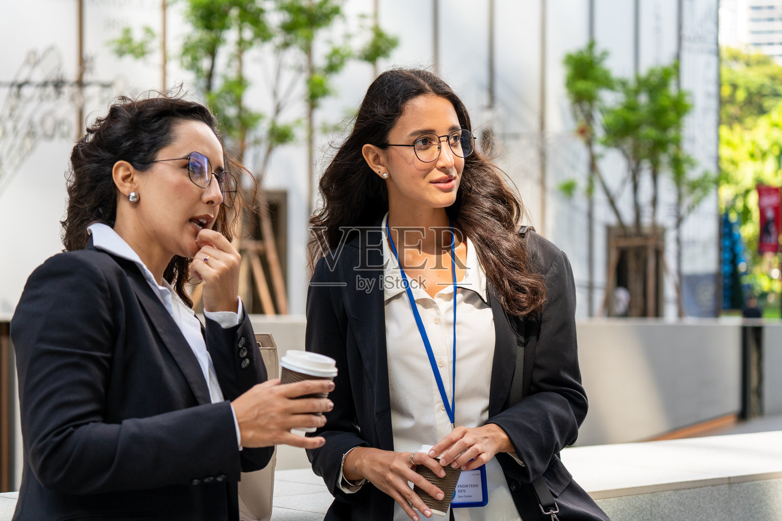 三位女商人在户外交谈并喝咖啡，展现了现代企业环境中的团队合作、沟通和专业协作。非常适合商业、领导力和职场概念。照片摄影图片