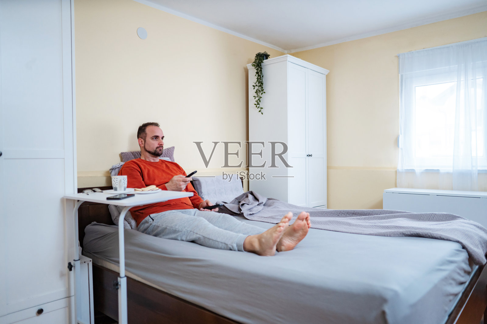 男人躺在床上看电视，享受早晨的放松时光照片摄影图片