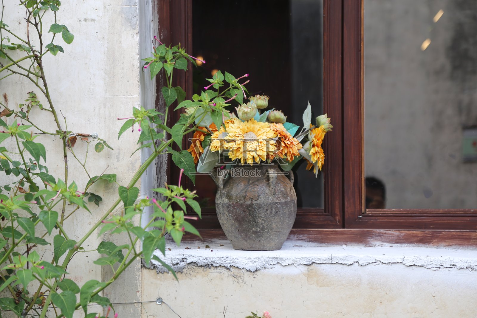 一个乡村风格的石头花瓶，里面插着黄色和橙色的花朵，摆放在一个老旧的窗台上照片摄影图片