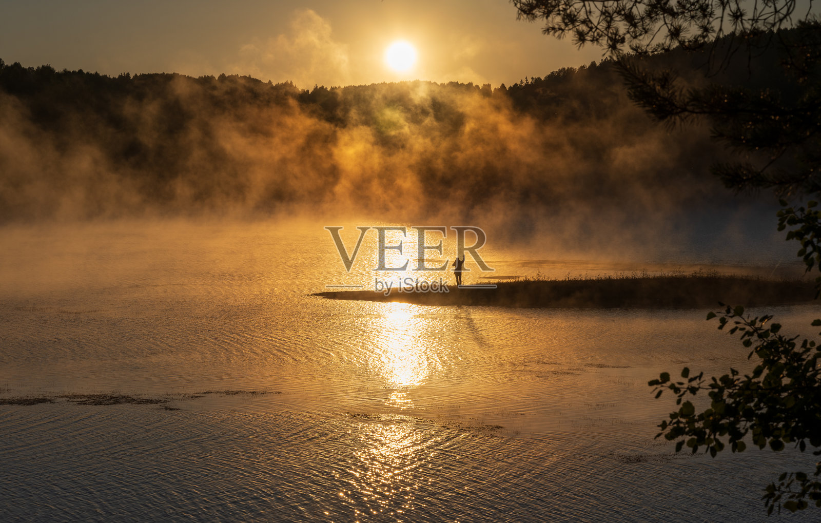 湖边半岛上摄影师的剪影，在日出时分，湖面上弥漫着薄雾，阳光穿透薄雾照亮水面。照片摄影图片