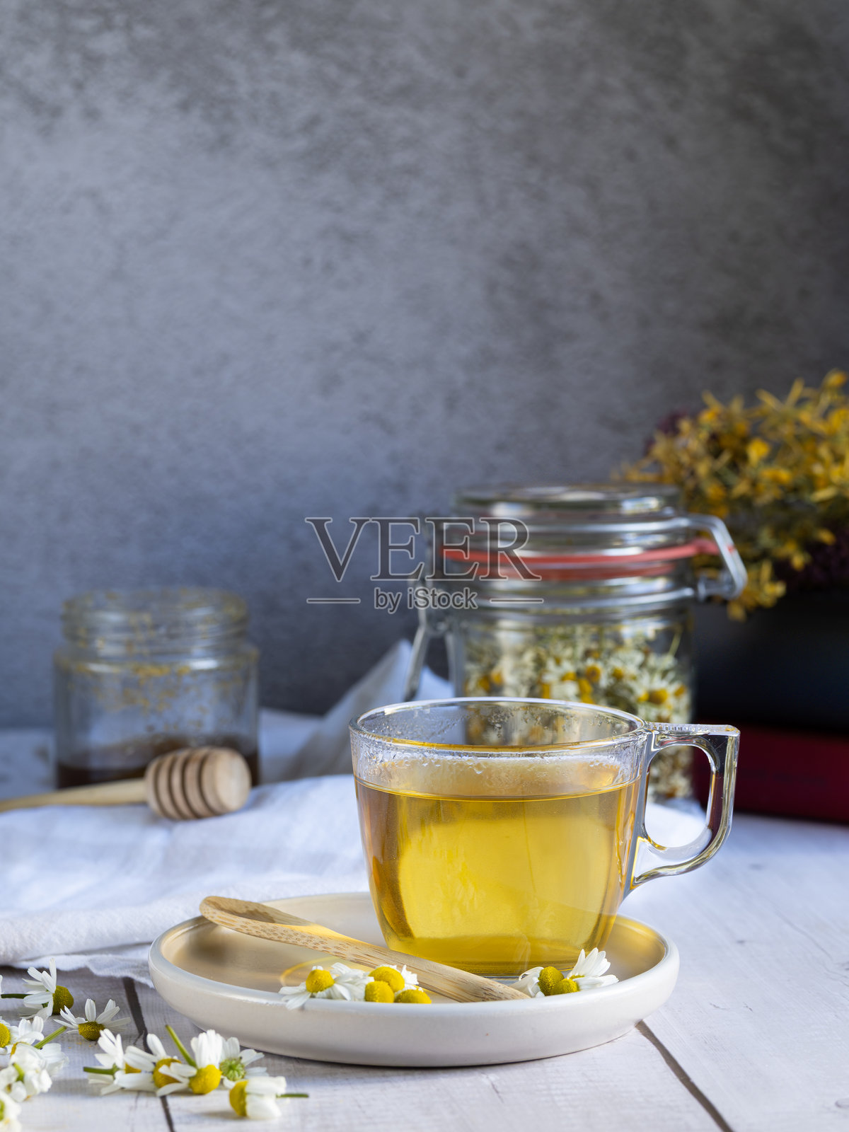 白木桌上放着一杯热洋甘菊茶，背景是干洋甘菊花和一本书照片摄影图片