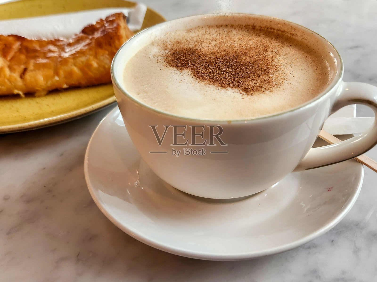 特写一杯卡布奇诺咖啡，上面撒着肉桂粉，旁边放着一份糕点。照片摄影图片