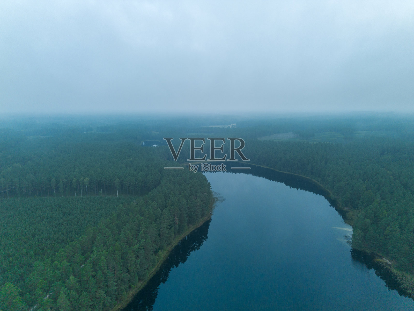 薄雾笼罩的蓝色湖泊和松树林的空中景象照片摄影图片