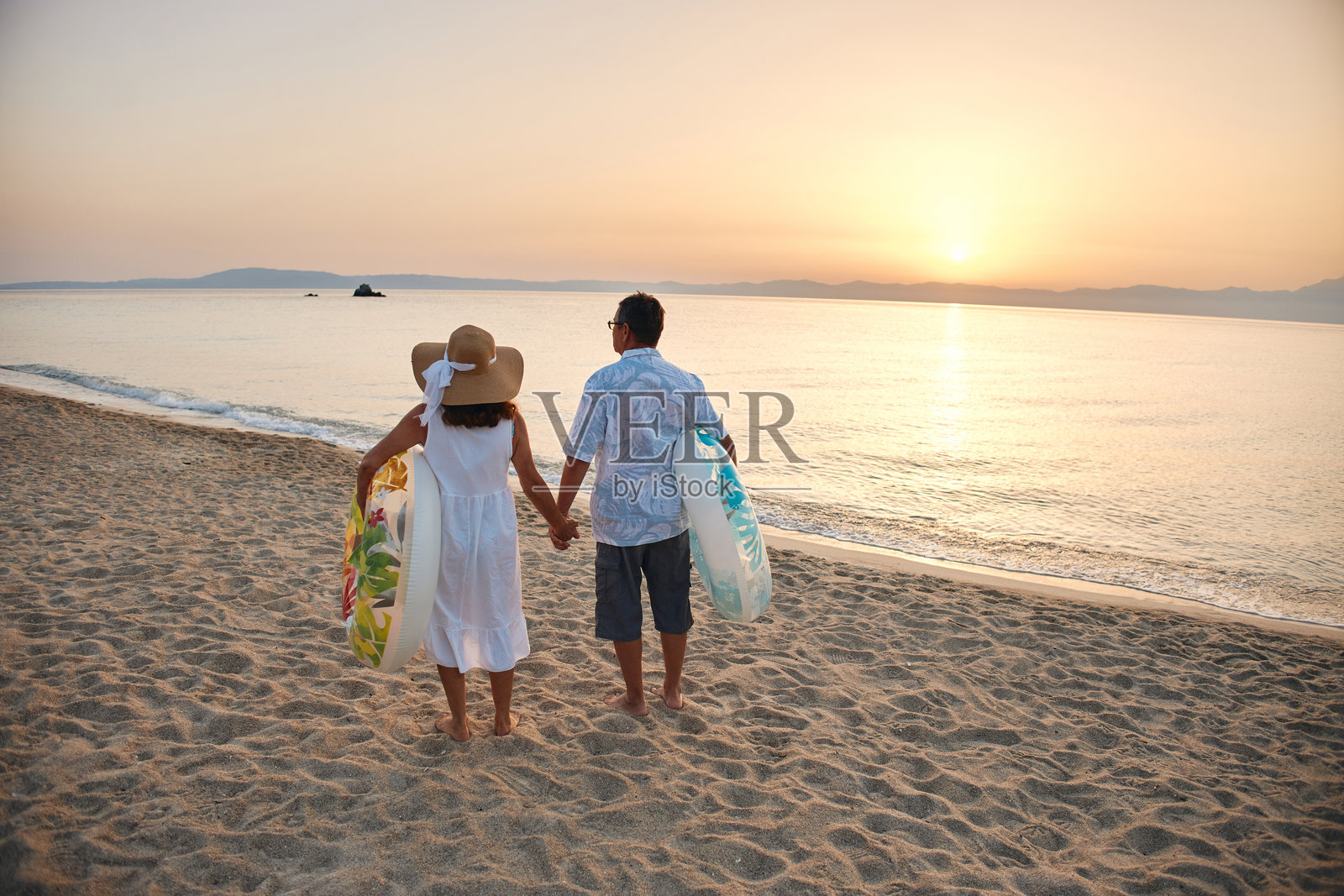 日落时分，一对成熟的夫妇手牵手在海滩上散步照片摄影图片