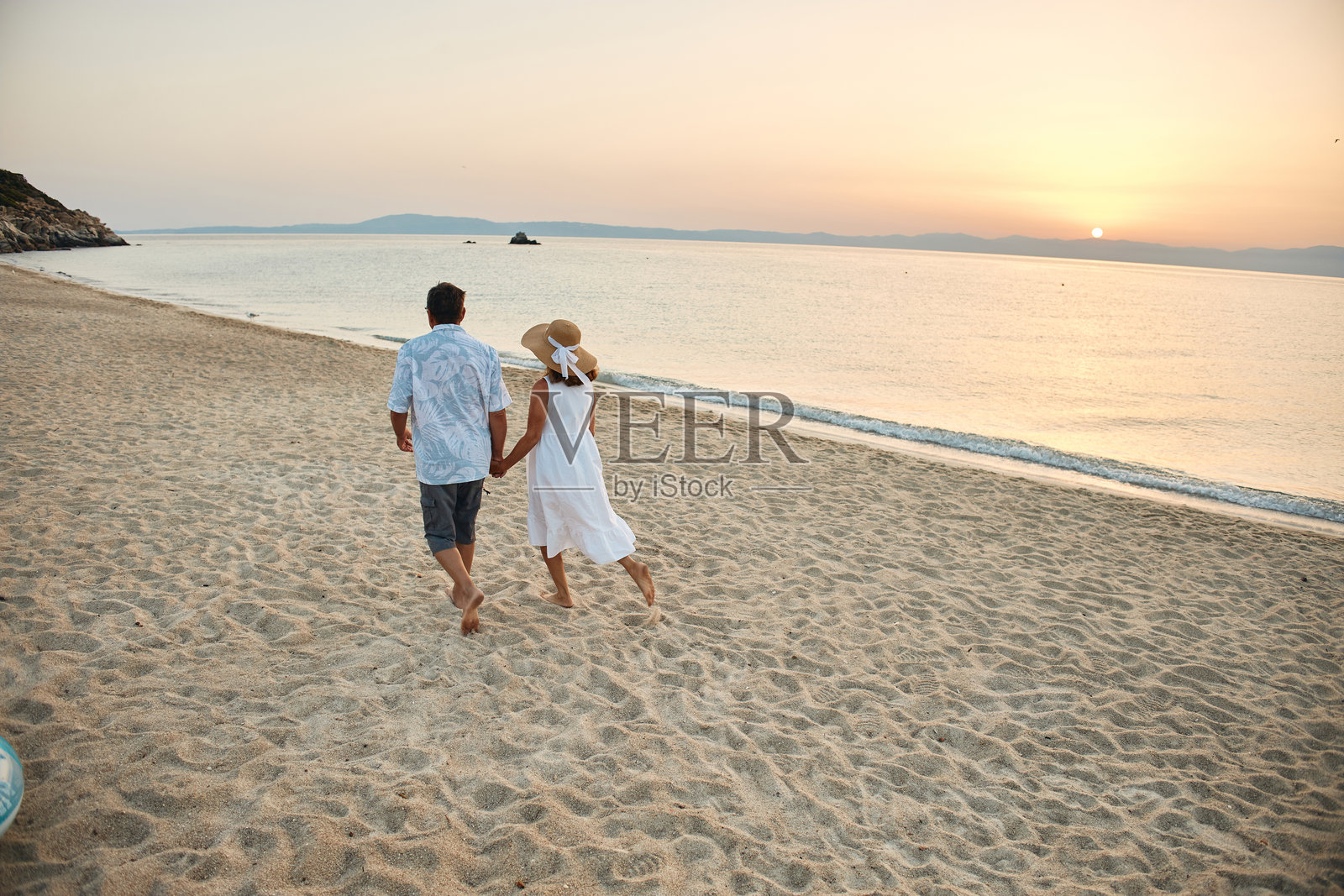 日落时分，情侣携手漫步在沙滩上照片摄影图片