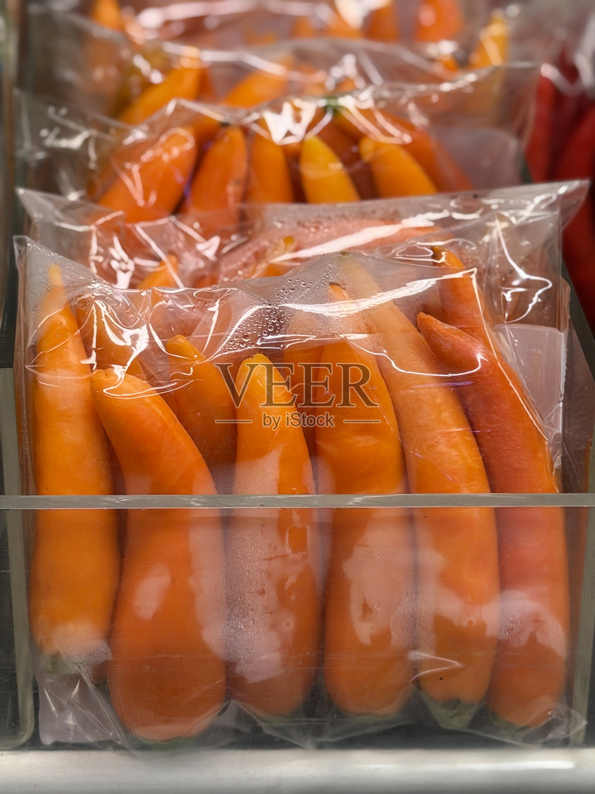 超市农产品展示的全画幅图像，预包装的橙色辣椒用塑料玻璃纸袋包裹，玻璃隔断屏风，聚焦前景，五种健康饮食概念照片摄影图片