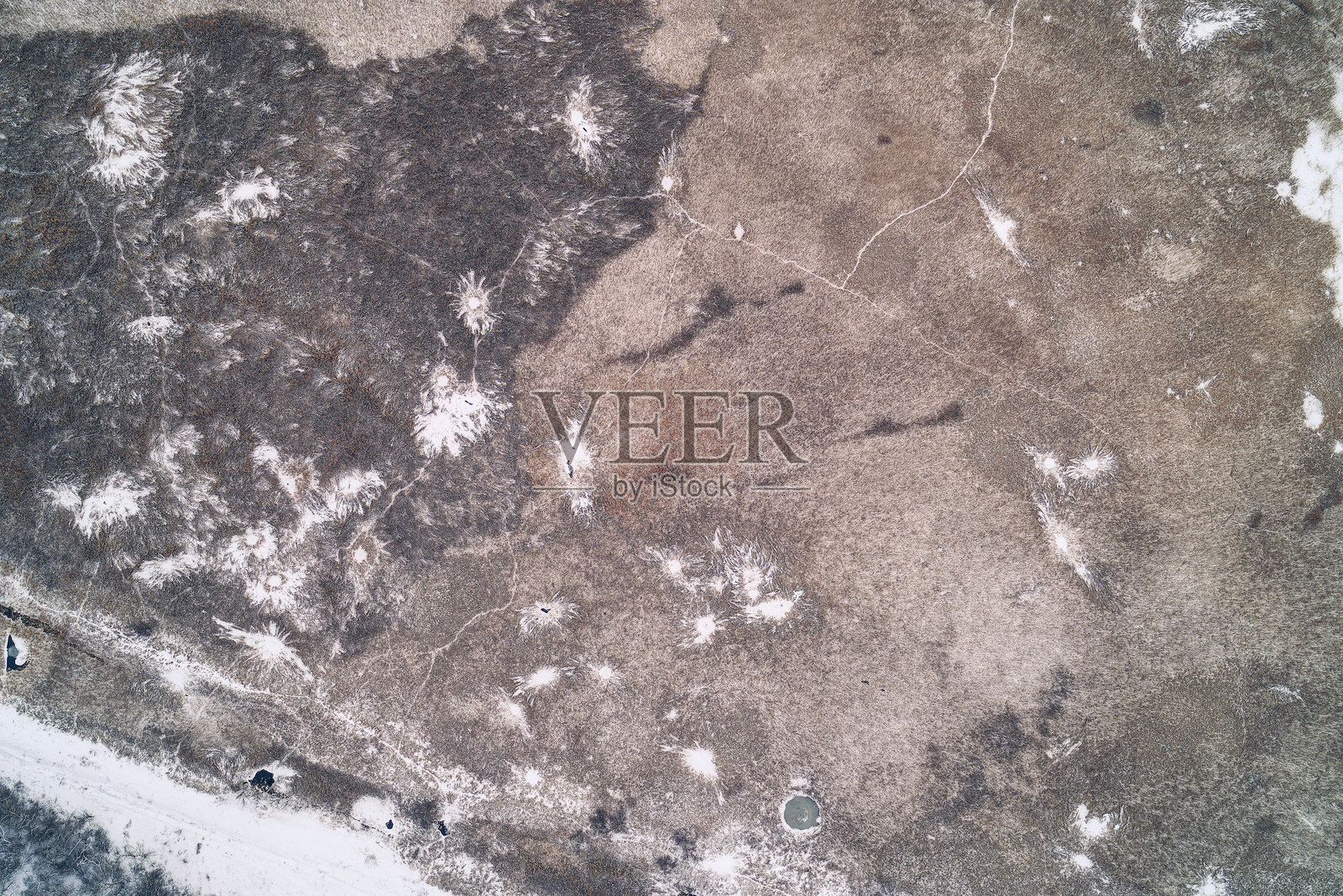 无人机俯瞰拍摄的冬季休耕农田，展现了粗糙的冻土纹理、霜冻痕迹和枯萎的植被照片摄影图片