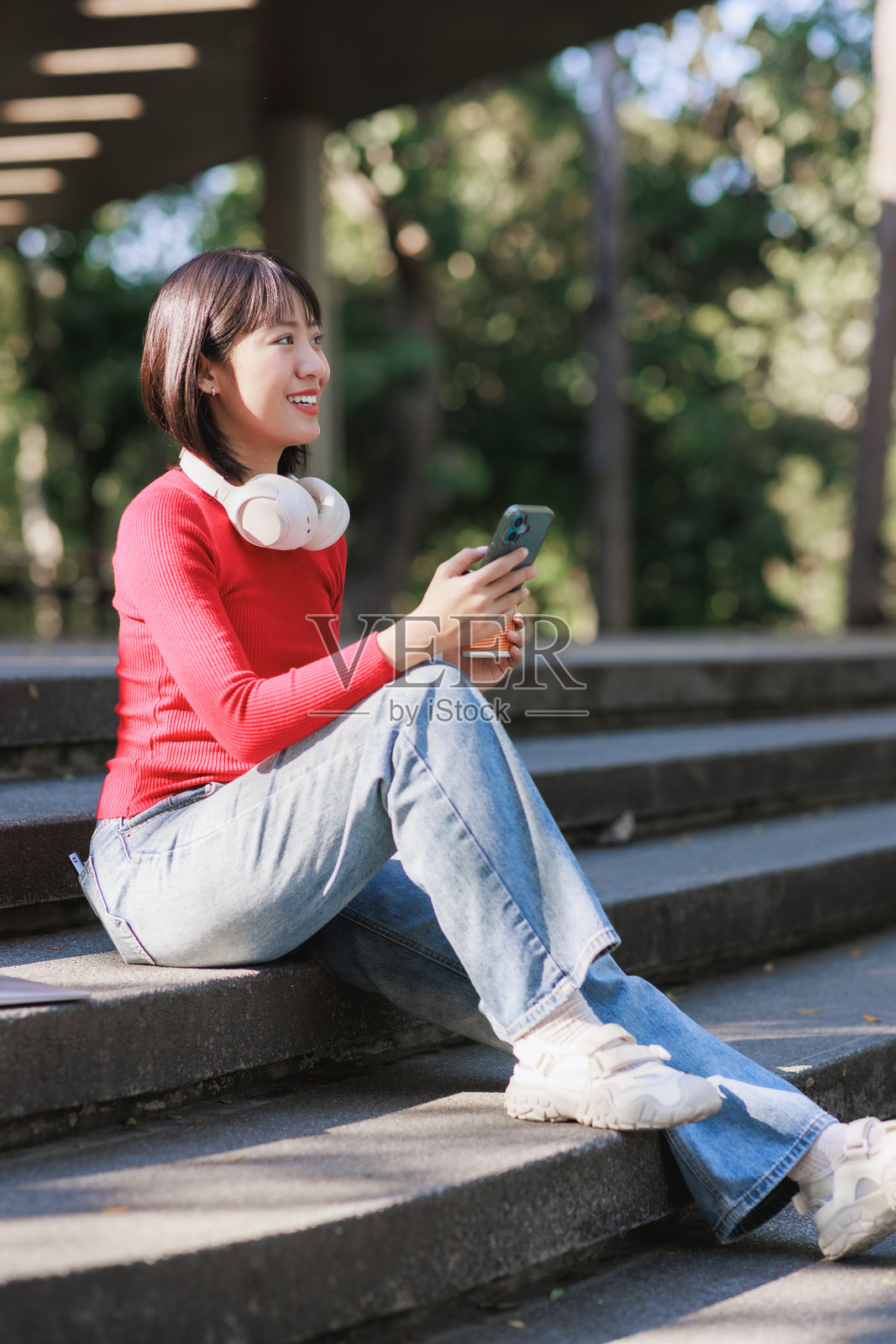 年轻女子在户外台阶上享受音乐和手机照片摄影图片