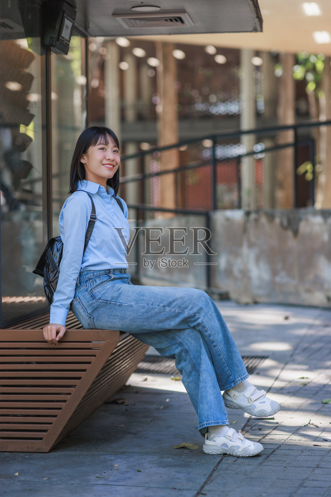 一位年轻的亚洲女性坐在公交车站，面带微笑照片摄影图片