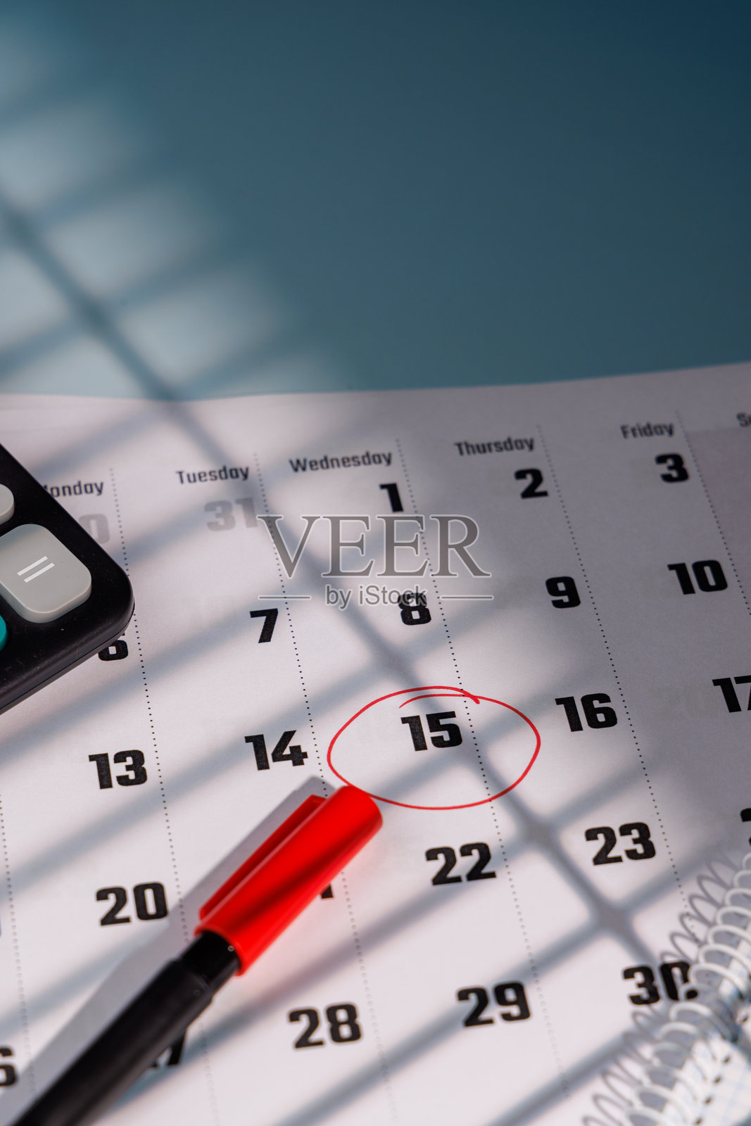 特写：日历上用红墨水标记的4月15日税务日，旁边放着计算器和钢笔，适用于会计和金融广告。照片摄影图片