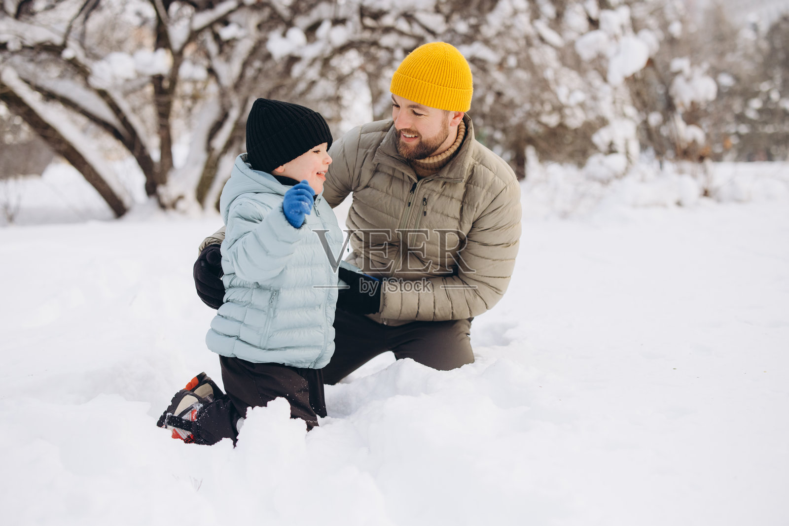父亲和儿子在雪地里玩耍，他们互相微笑，在冬天里增进感情。照片摄影图片