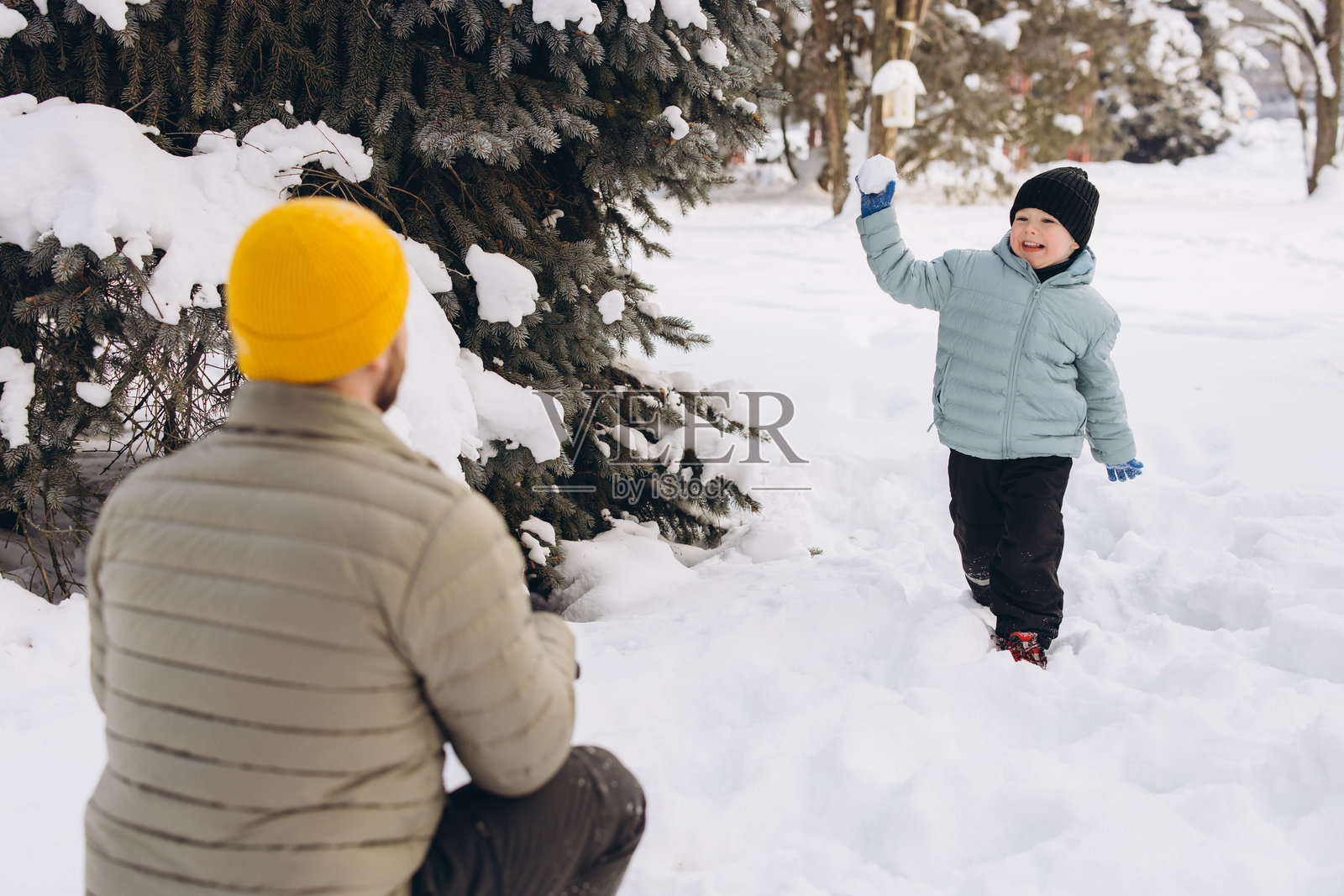 父亲和儿子在雪地公园里开心地玩雪球，共创快乐的冬日家庭回忆照片摄影图片