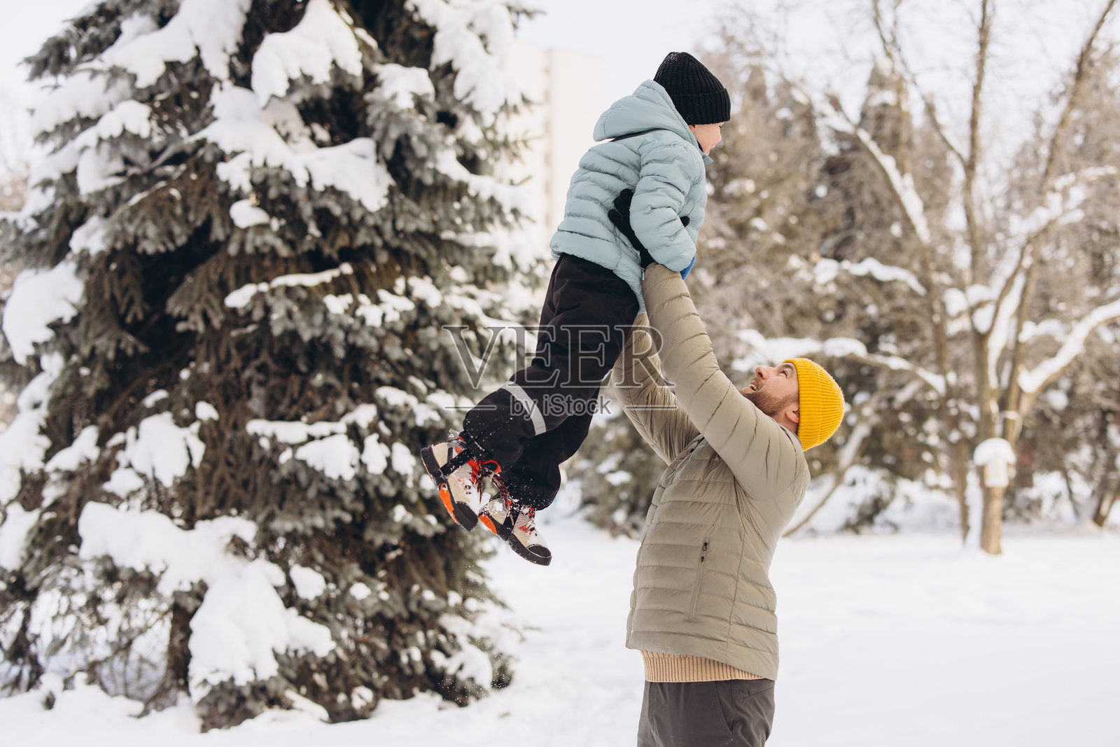 快乐的父亲在冬日雪林公园里举起儿子，玩耍嬉戏，享受户外家庭时光照片摄影图片