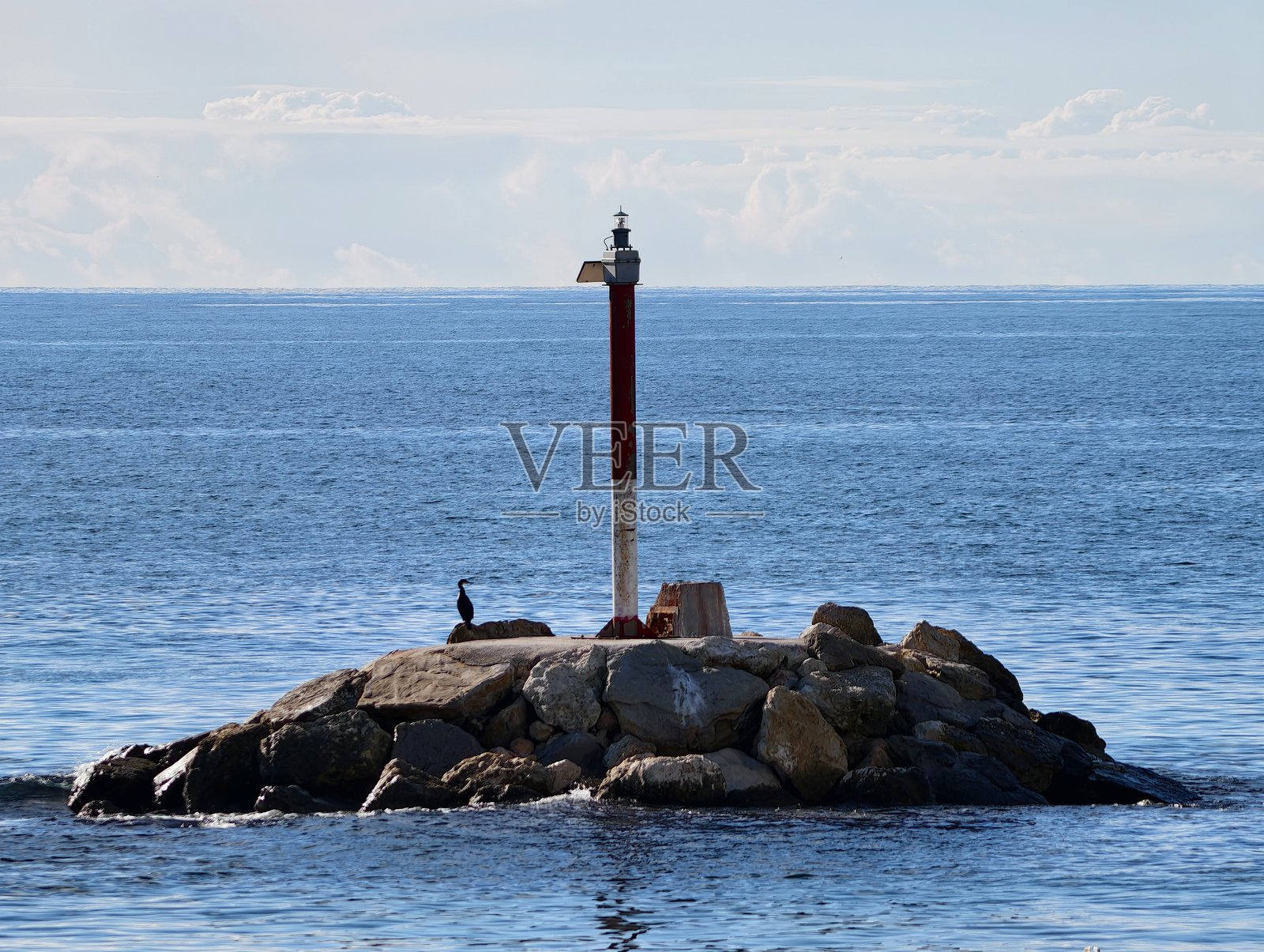 宁静的海景，展示了孤零零的灯塔，周围环绕着纹理岩石和平静的海水。照片摄影图片