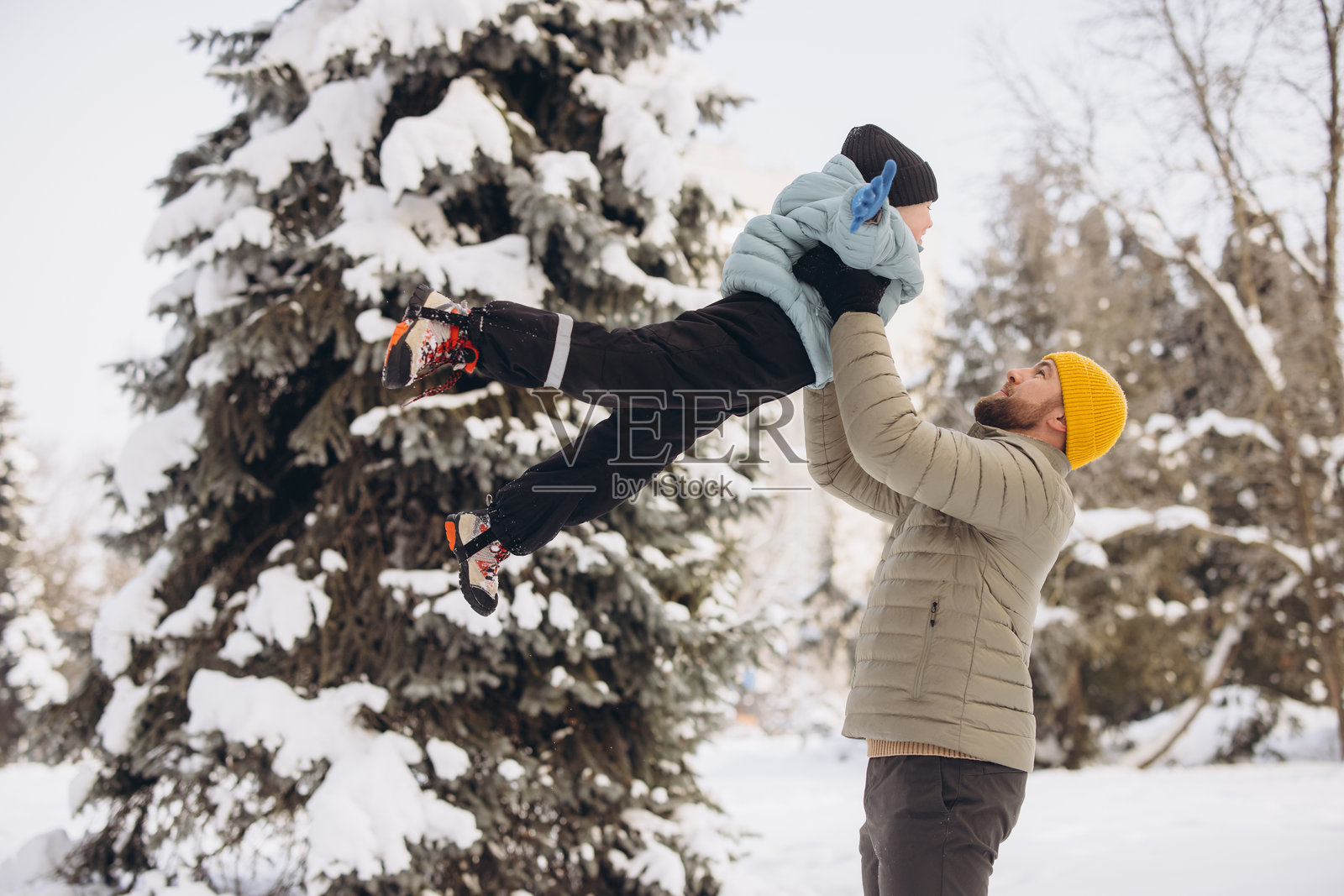 父亲在雪天的户外，将儿子高高举起，享受着亲子时光，共享欢乐的家庭时刻。照片摄影图片