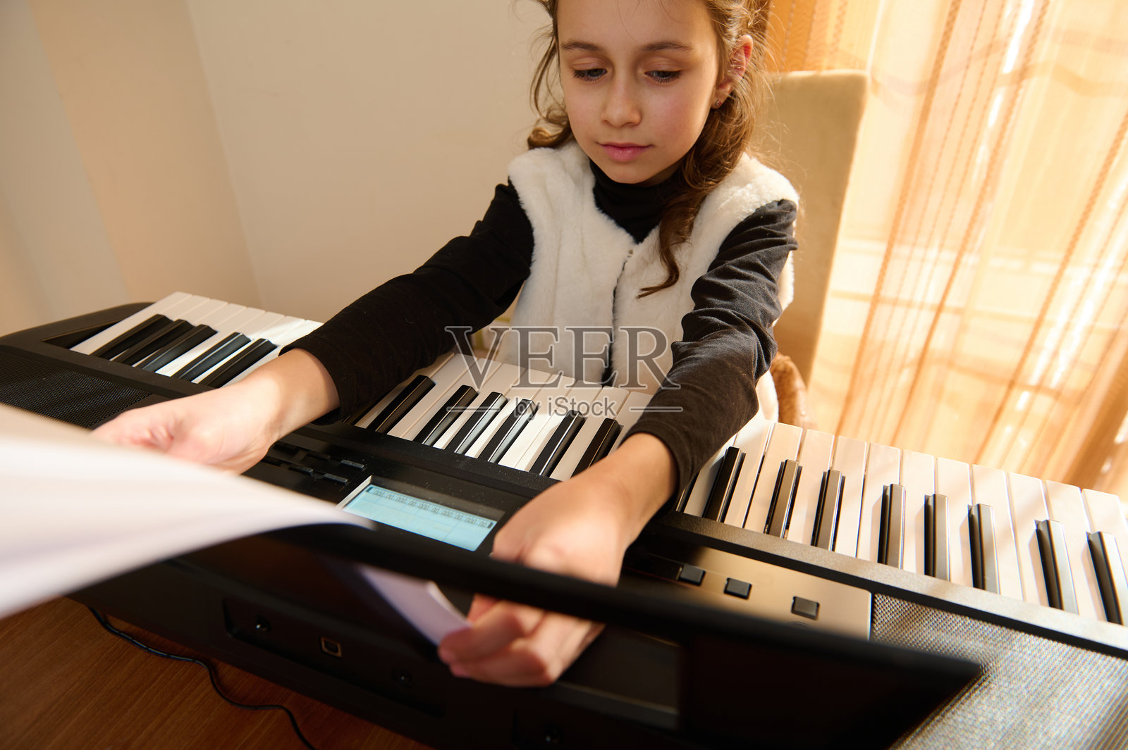 小女孩在家弹奏合成器键盘，沉浸在专注的音乐晨练中，温馨的家庭时光照片摄影图片