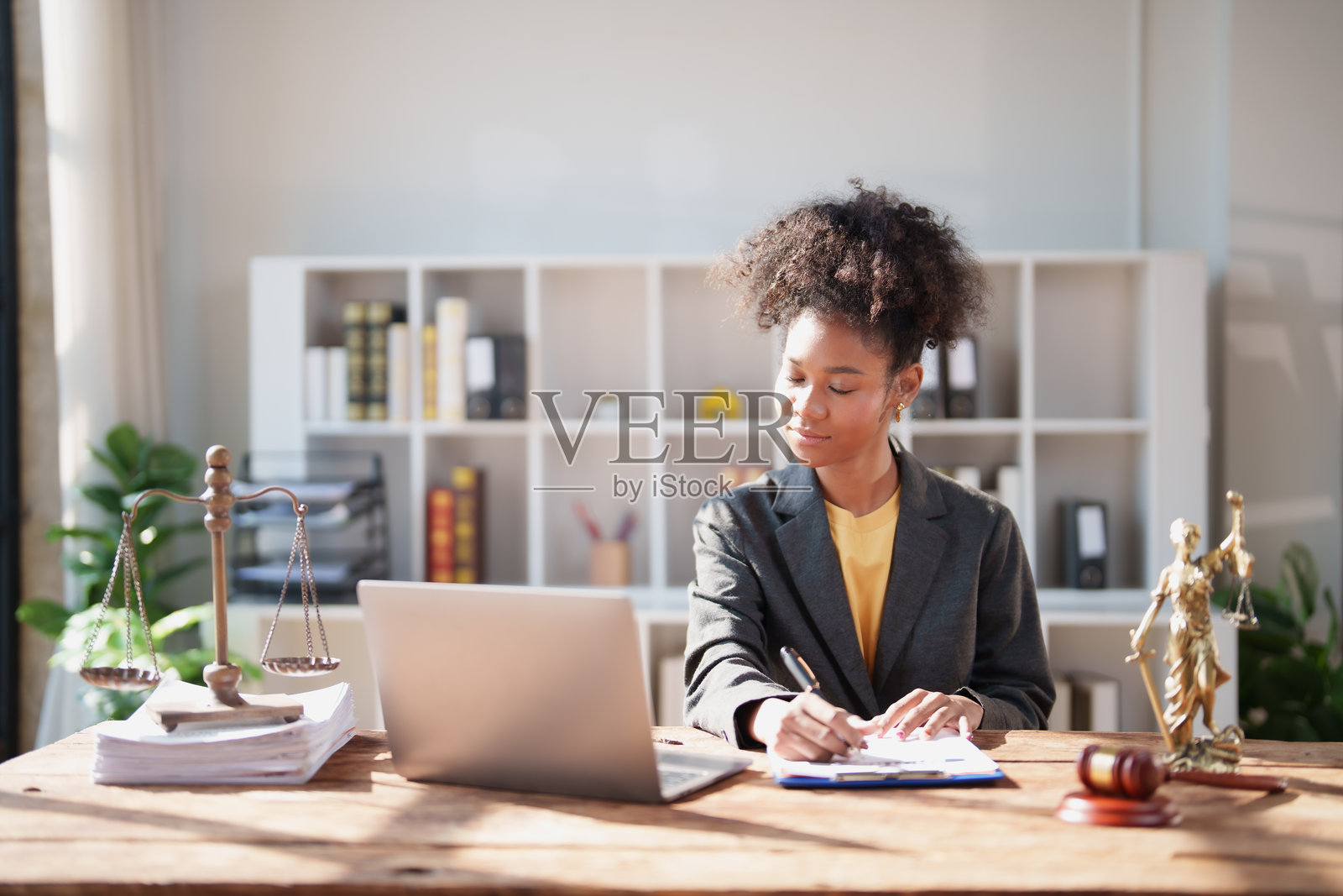 一位穿着西装的年轻黑人女律师正在现代律师事务所的办公桌前，专注于法律文件、天平、法槌，准备案件。照片摄影图片