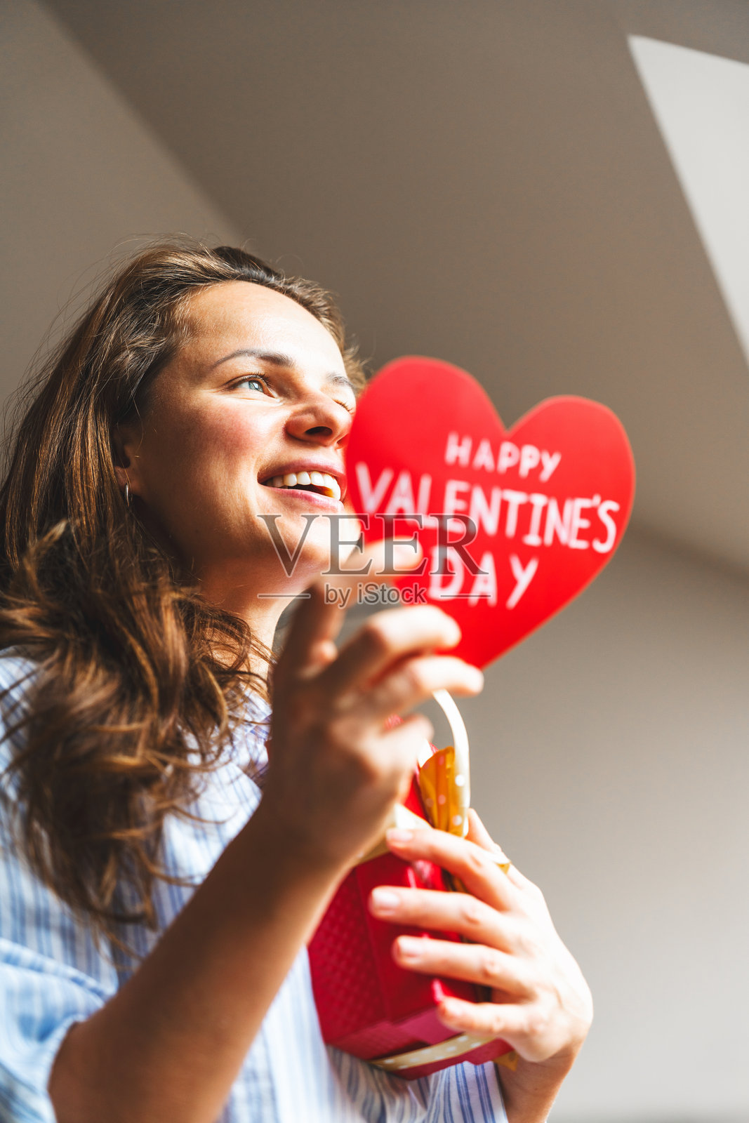 一位面带微笑的女性，手持心形情人节贺卡。照片摄影图片