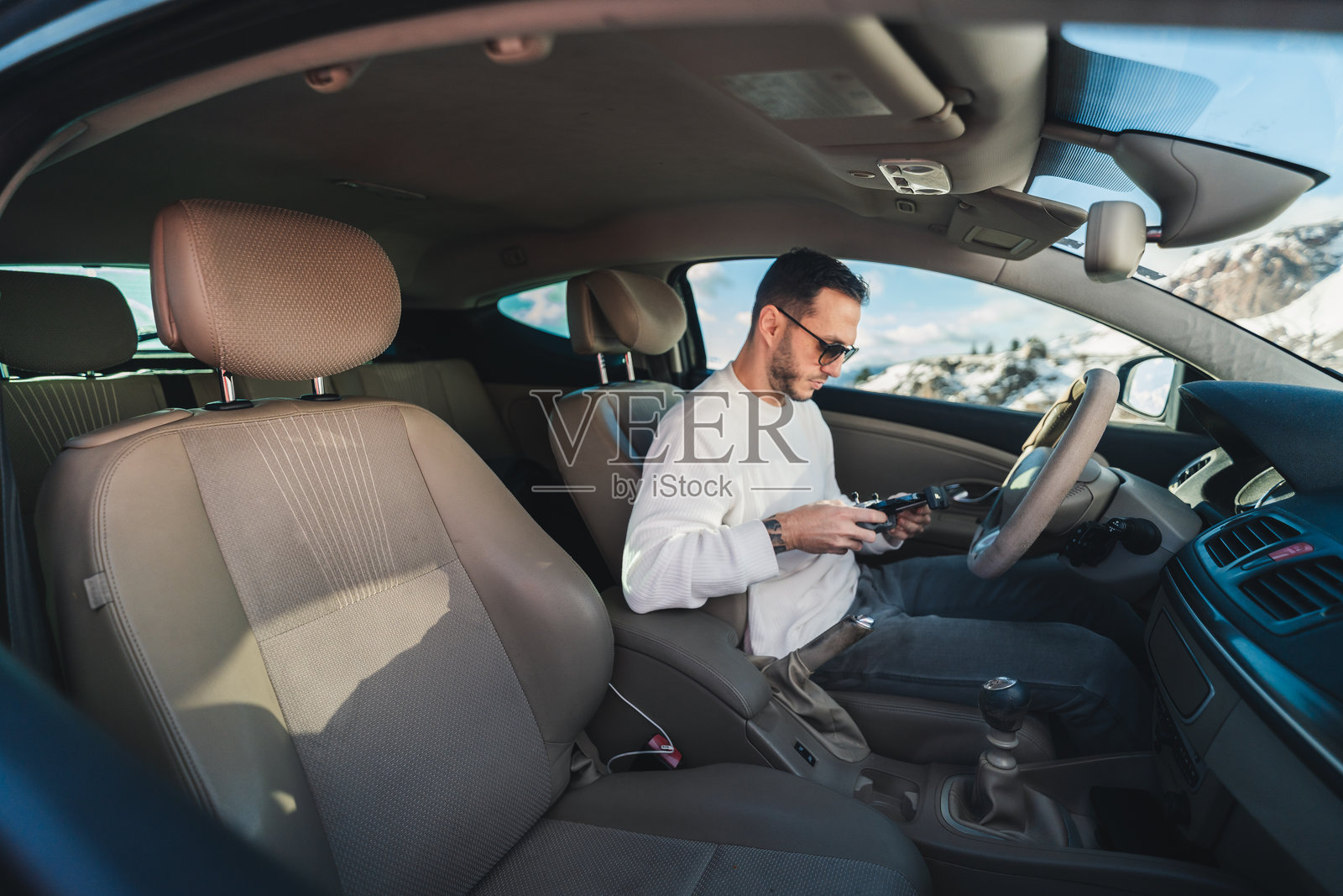 男子在车内手持无人机遥控器，车窗外是冬季的山景照片摄影图片