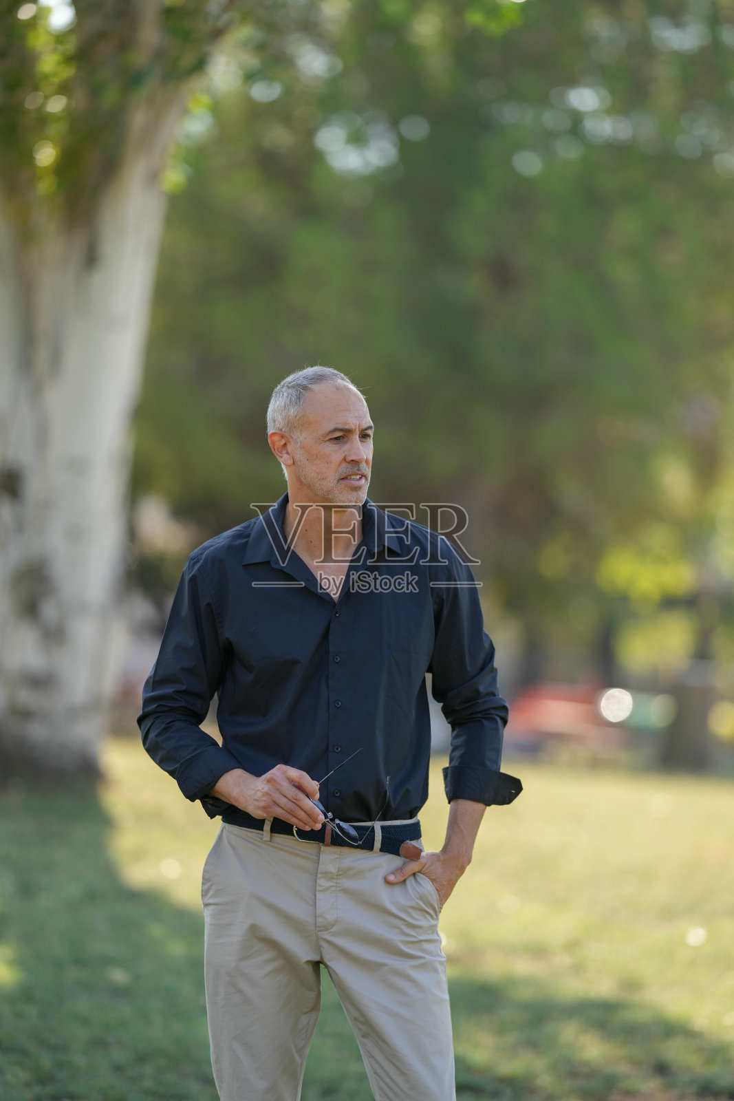 一个穿着黑色衬衫和卡其色裤子的男人正站在公园里照片摄影图片