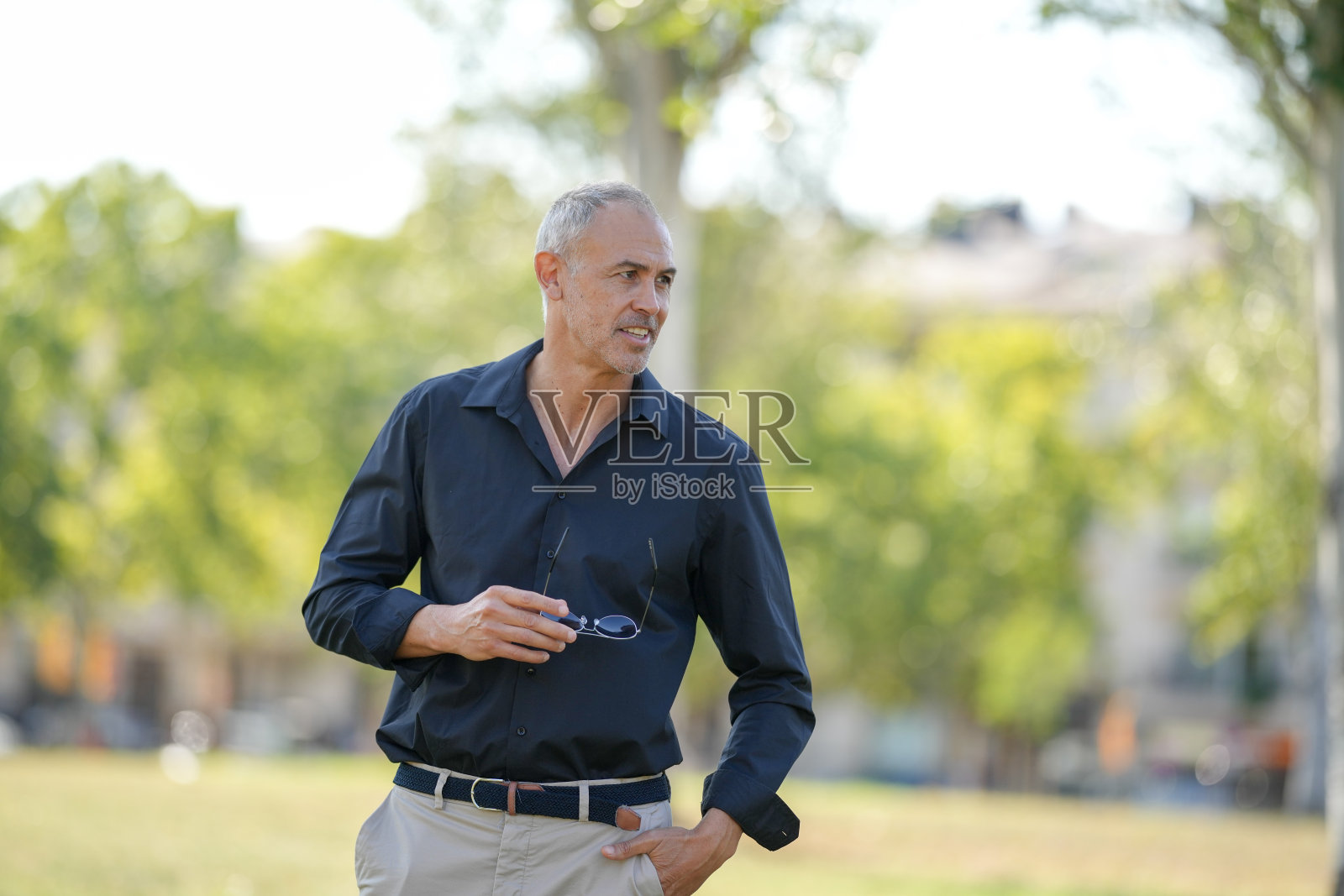 一个穿着黑色衬衫和卡其色裤子的男人正站在公园里照片摄影图片