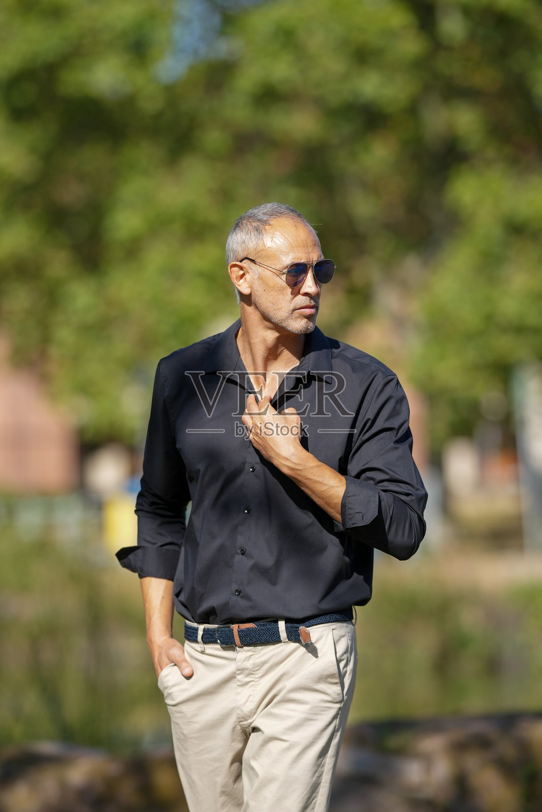 一个穿着黑衬衫和卡其色裤子的男人正在公园里散步照片摄影图片