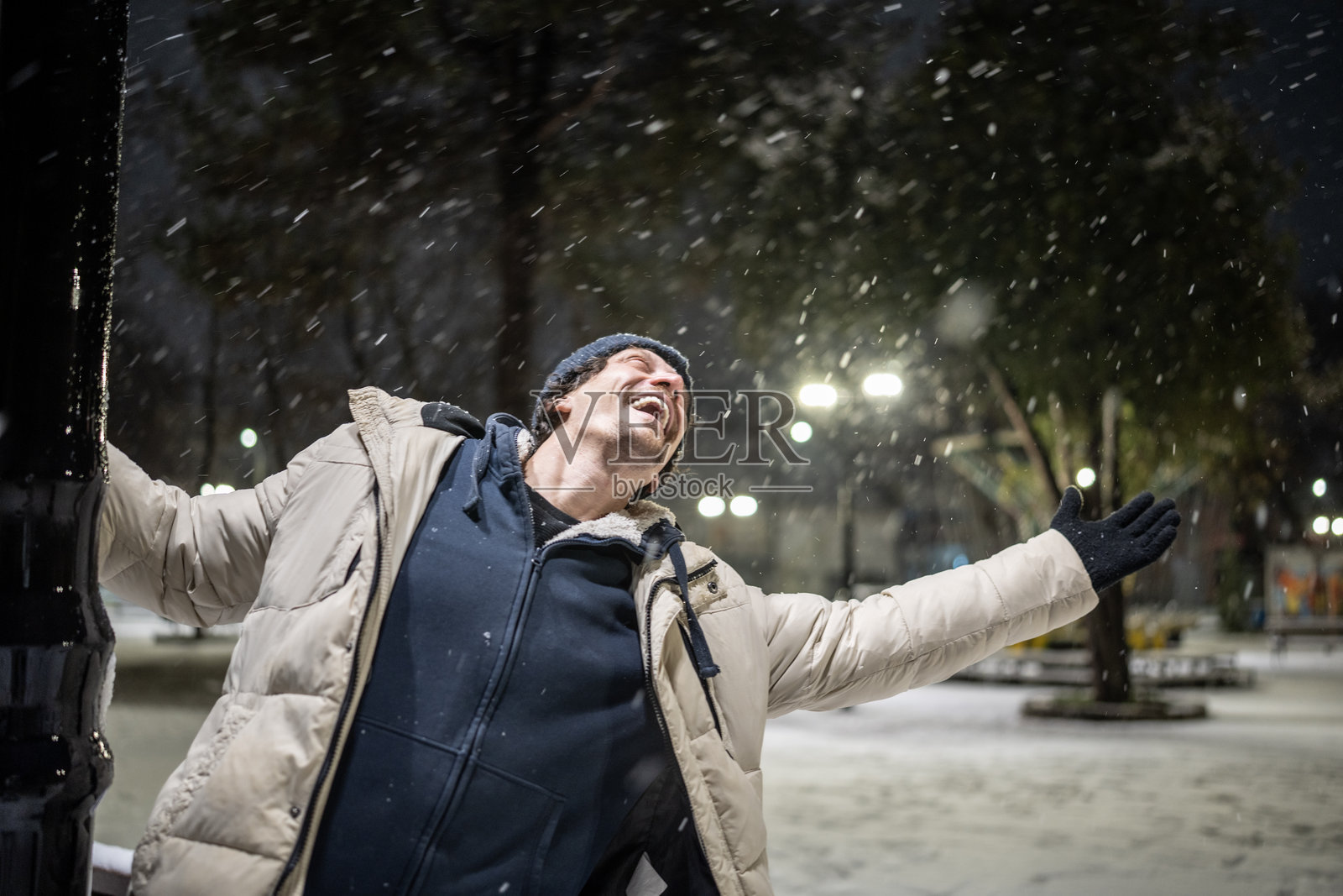 夜晚，一名男子在户外的雪中张开双臂，脸上洋溢着喜悦照片摄影图片