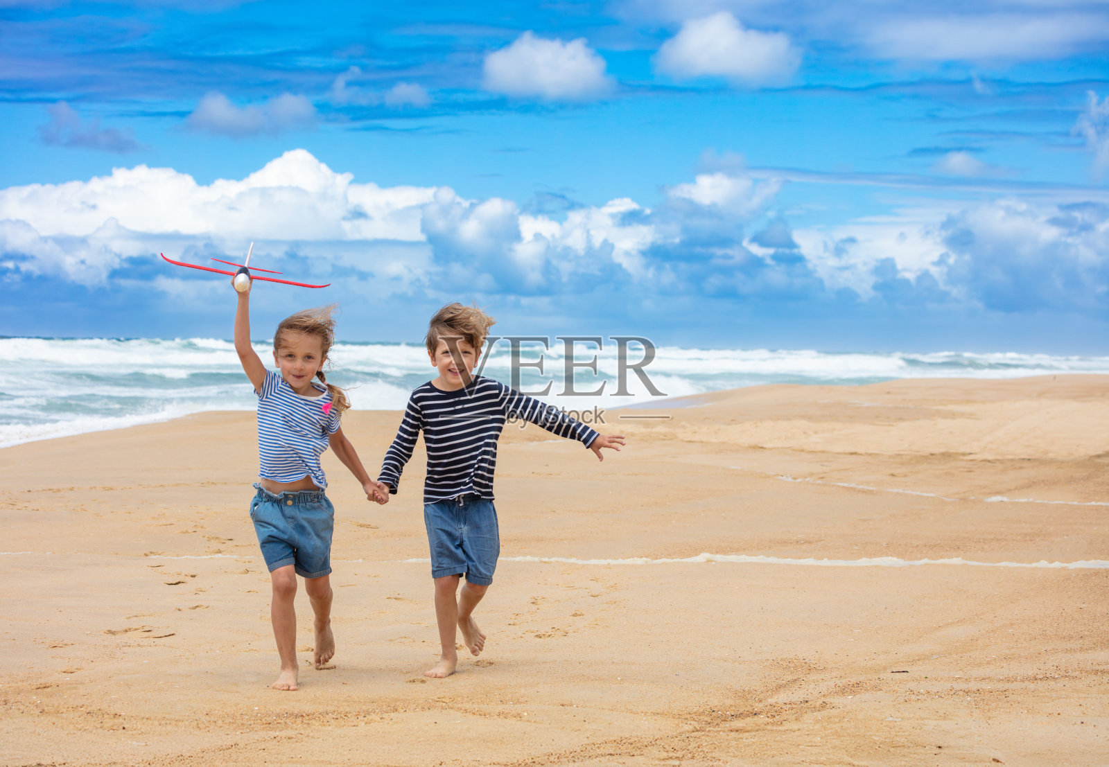 快乐的孩子们牵着手在沙滩上奔跑，手里拿着玩具飞机照片摄影图片
