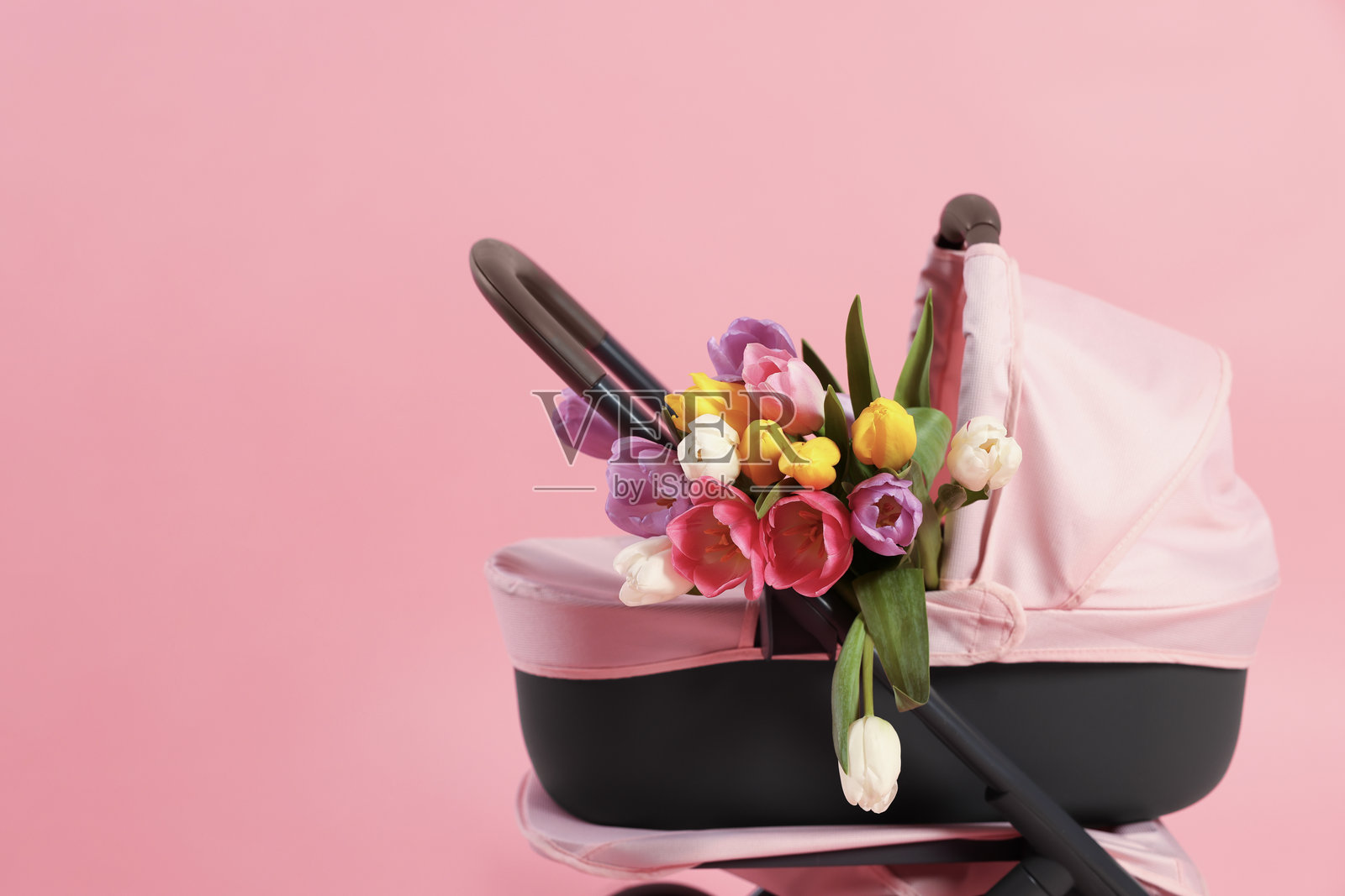 粉色背景上的时尚娃娃推车和郁金香，留有文字空间。儿童玩具照片摄影图片