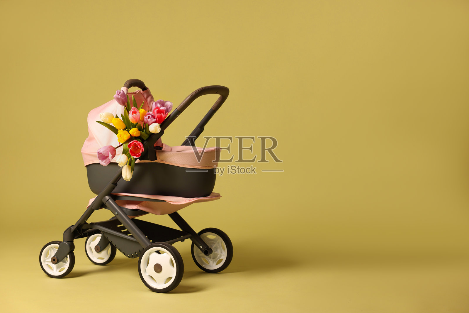 时尚的娃娃推车和郁金香在橄榄色背景上，留有文字空间。儿童玩具照片摄影图片