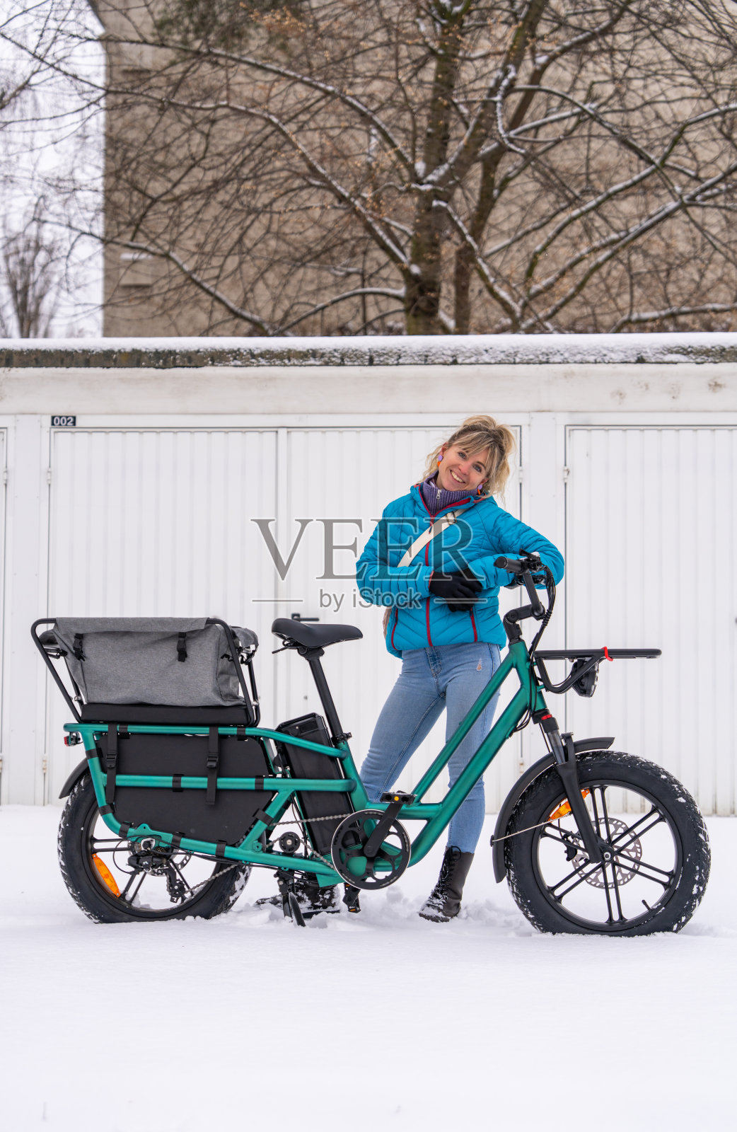 快乐的女性在雪天的城市街道上骑着电动货运自行车。可持续的城市交通、环保出行、现代生活方式和绿色交通理念。照片摄影图片