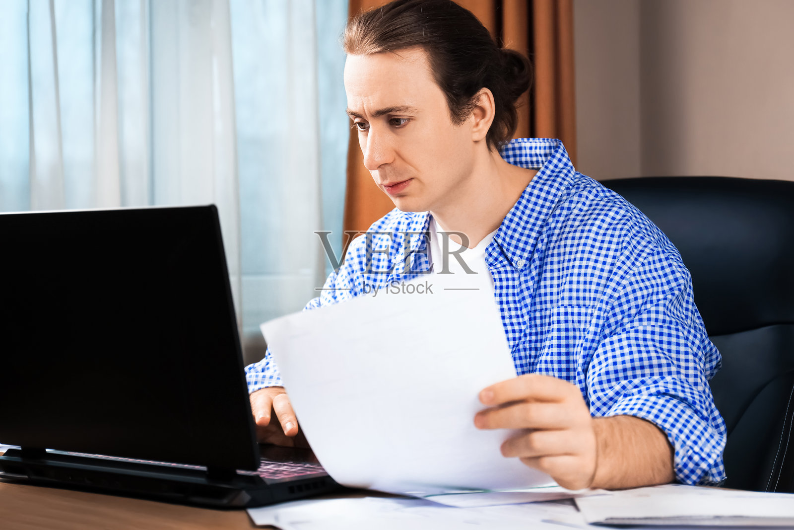 一名男子在笔记本电脑前认真查看文件。居家办公、支付账单和企业管理的远程工作概念照片摄影图片