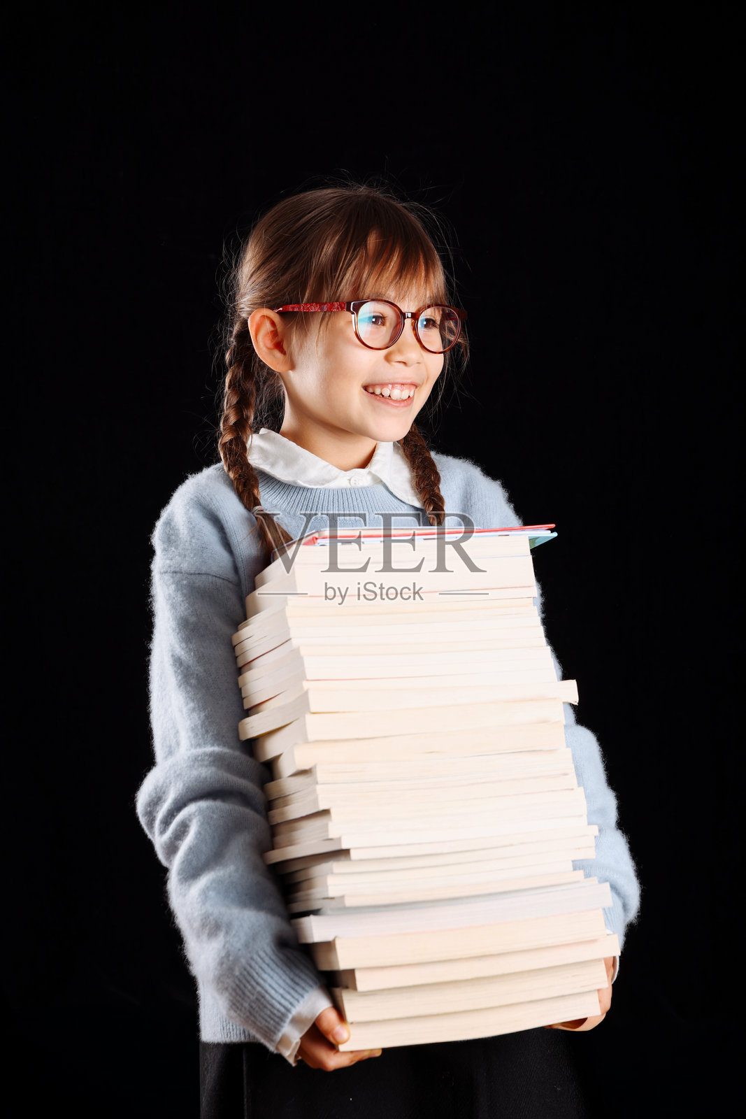 小女孩在身前抱着一大摞书，在影棚的黑色背景前拍摄照片摄影图片