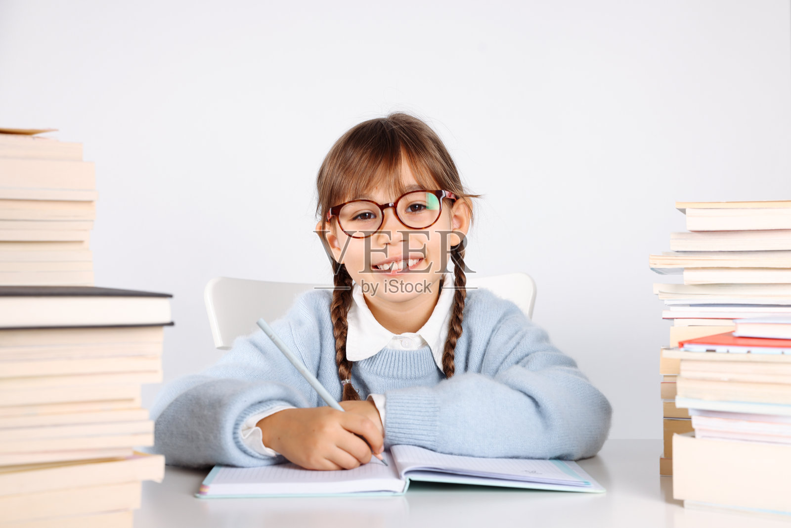 扎着辫子、笑容灿烂的金色头发小学生，手里拿着叠起来的书照片摄影图片