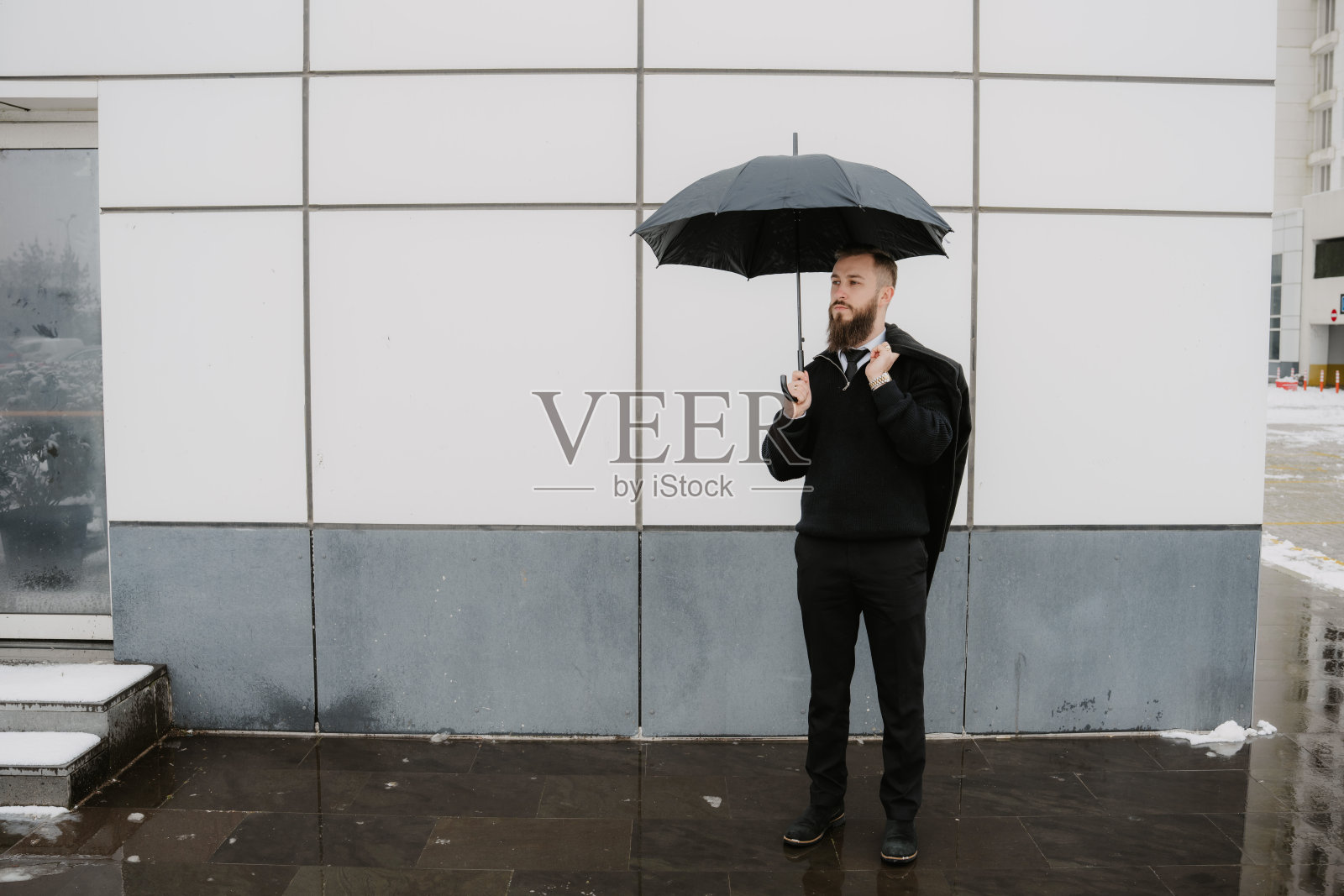 身着优雅西装的商界男士，撑着雨伞，站在现代风格的墙壁前照片摄影图片