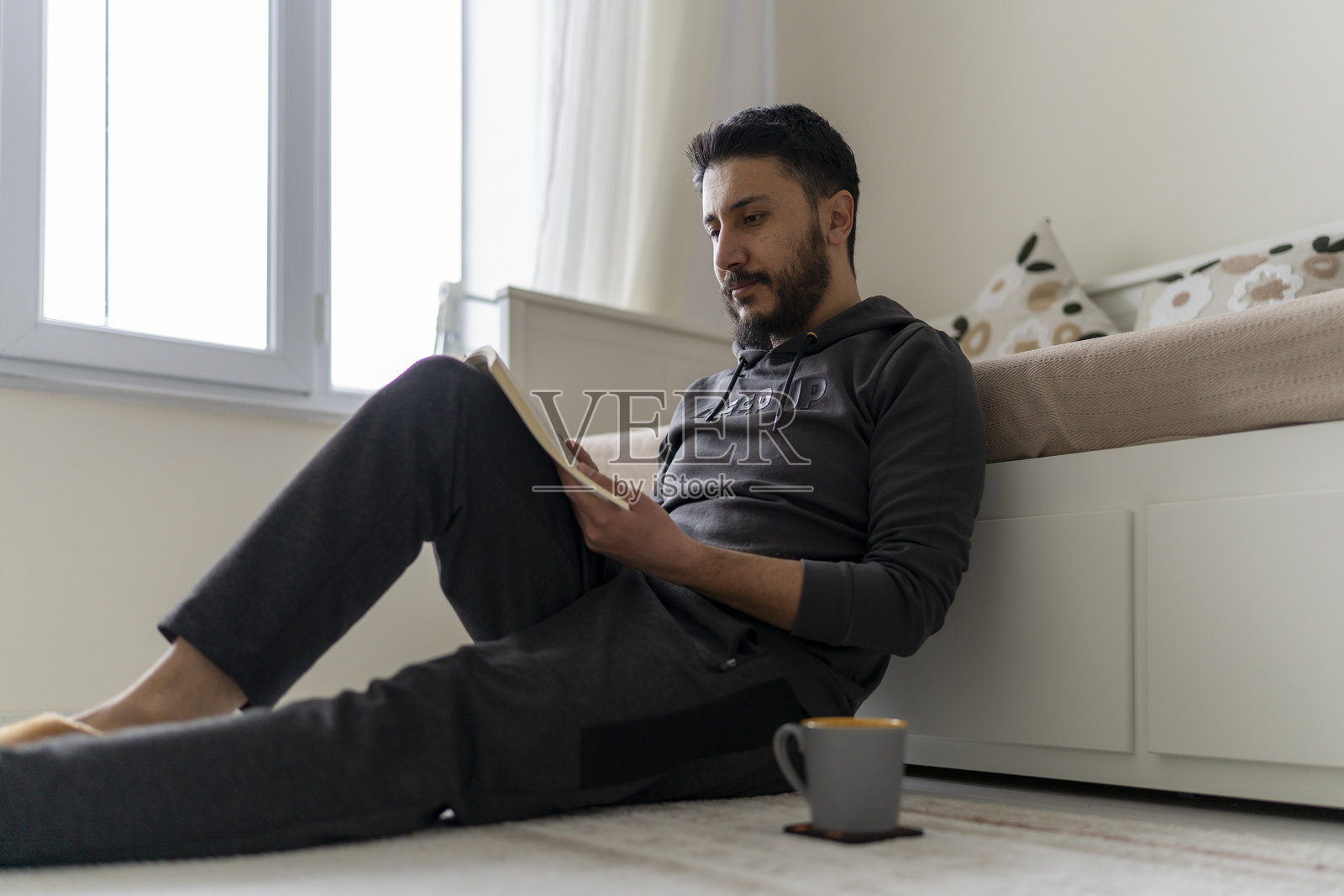 一位年轻男子在家中一边喝咖啡一边平静地阅读书籍。照片摄影图片