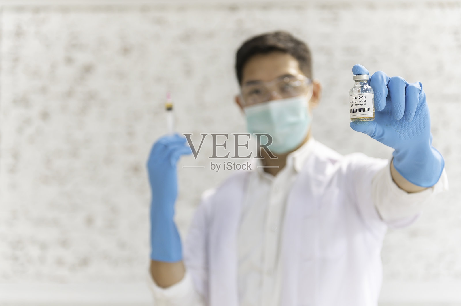 身穿白大褂的医生戴着蓝色防护手套，手持装有疫苗的注射器，准备进行注射。照片摄影图片