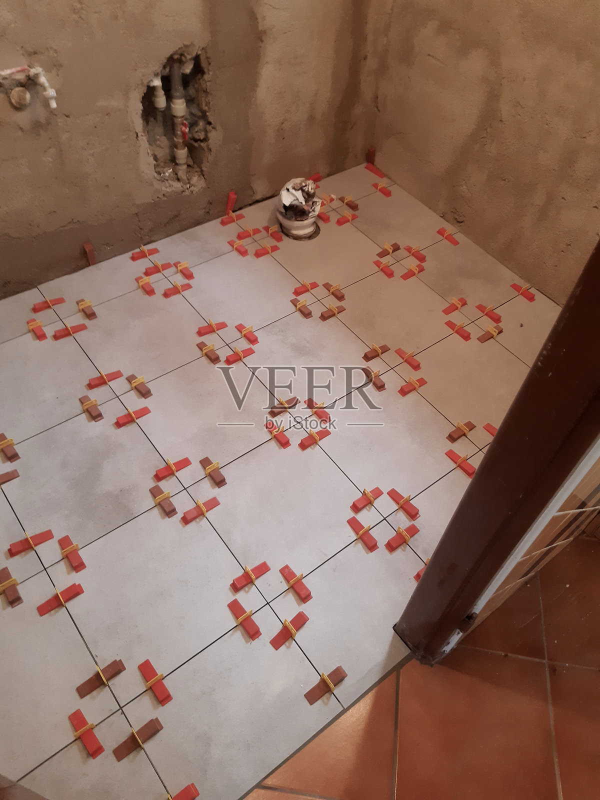 捕捉到使用瓷砖调平系统铺设瓷砖的过程。该系统由一次性夹子（红色部分）和可重复使用的楔子（黄色部分）组成，可确保瓷砖表面完全平整，接缝宽度均匀。背景照片摄影图片