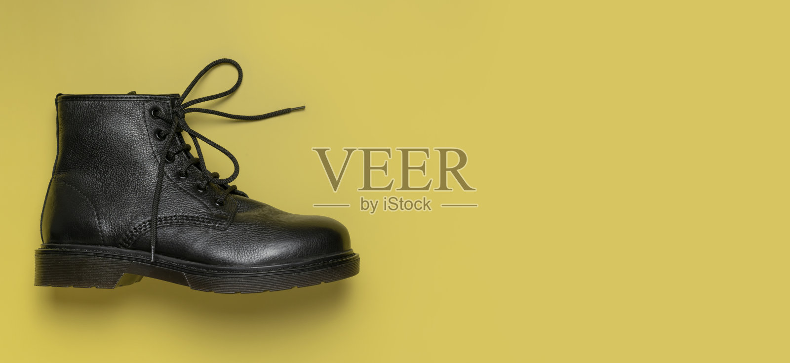 时尚青年黑色皮革秋季靴子，黄色背景，俯视平面图。时尚男女通用垃圾摇滚靴带鞋带。服装、鞋子、时尚背景。经典皮革鞋照片摄影图片