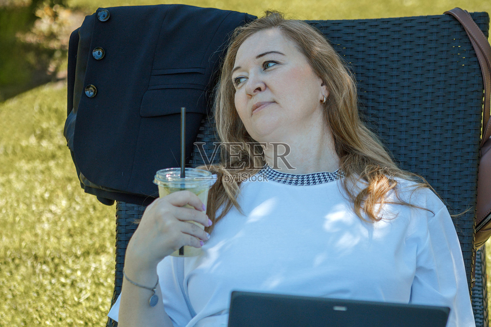 一位金发中年女性在花园的躺椅上用笔记本电脑工作，绿色居家办公概念。照片摄影图片