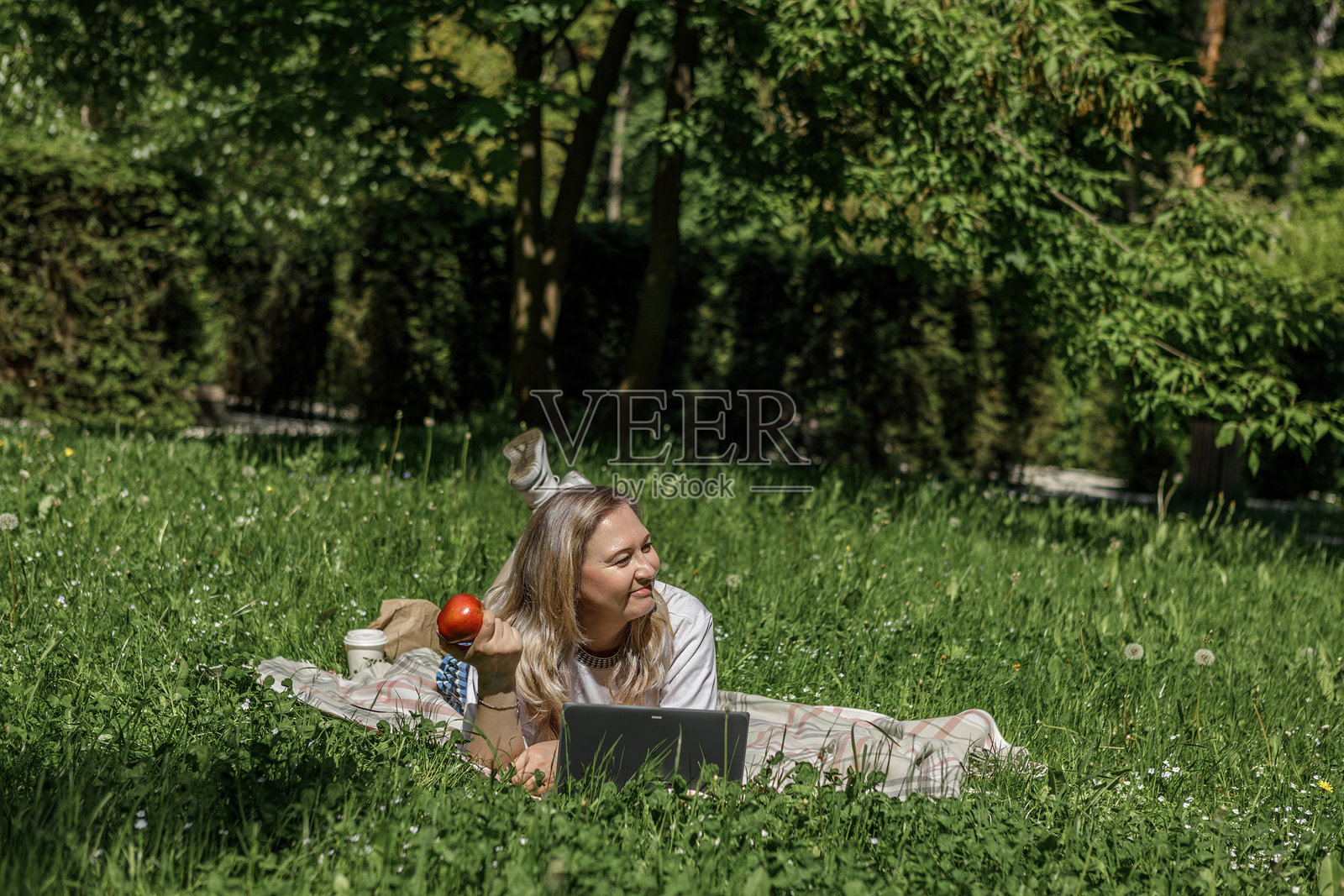 一位金发中年女子在花园的躺椅上使用笔记本电脑工作，绿色家居办公概念。照片摄影图片