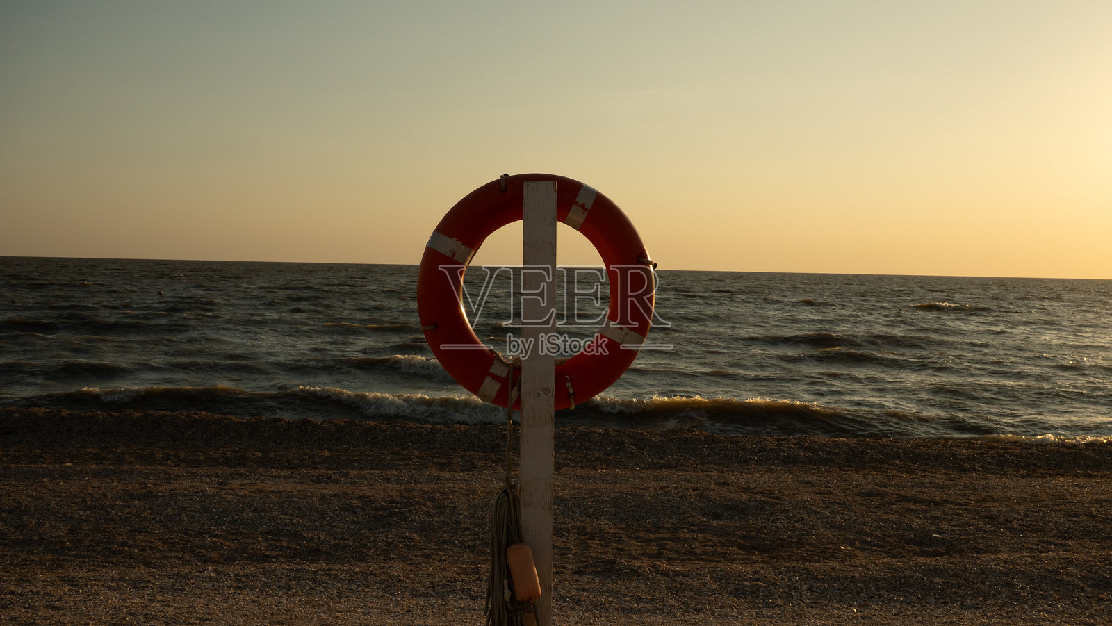 在温暖的黄金时刻，救生圈悬挂在木桩上，背景是宁静的海洋和轻柔的波浪，象征着海滩上的救赎与援助。照片摄影图片