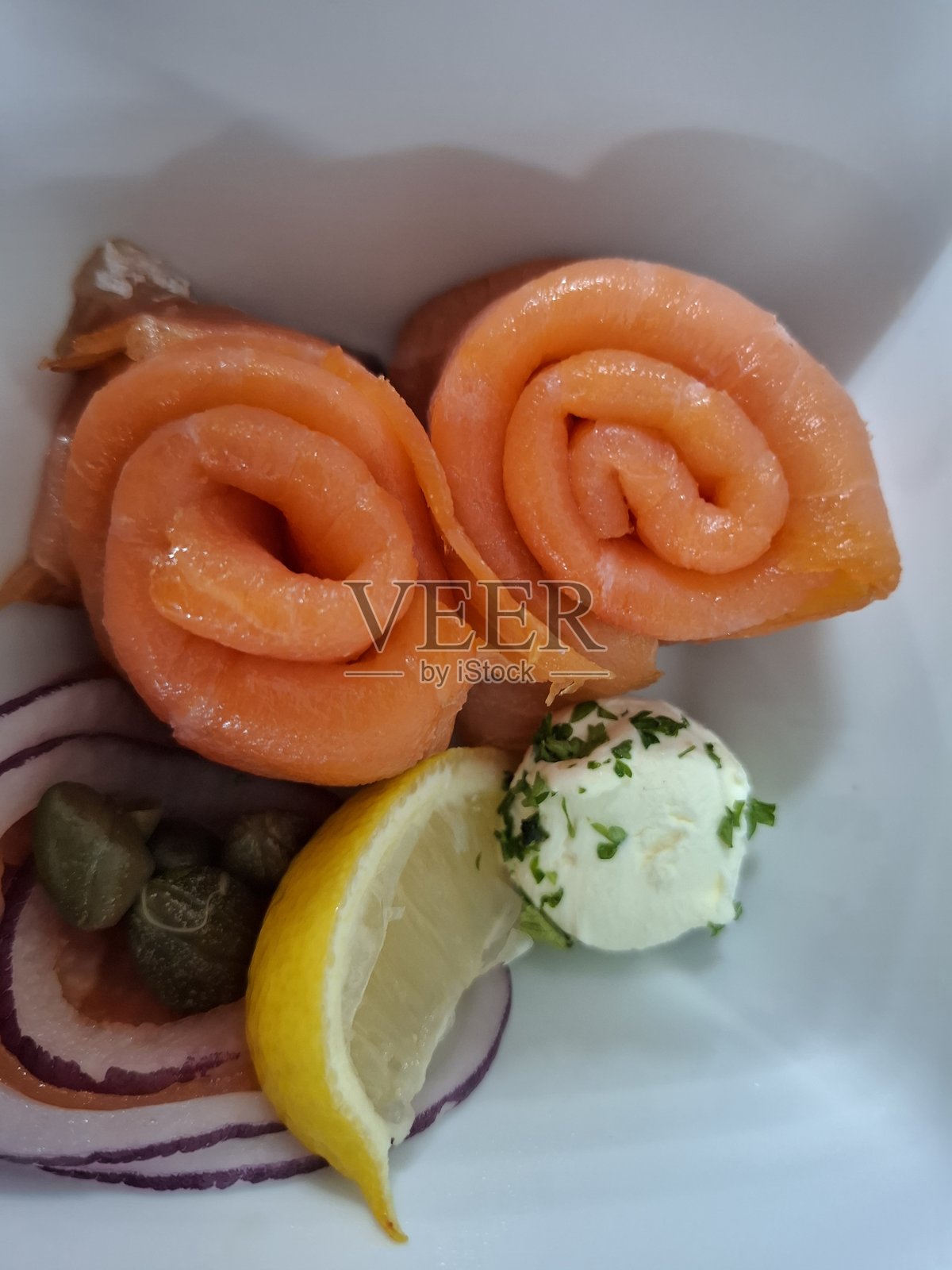 烟熏三文鱼玫瑰配柠檬角、红洋葱片和香草黄油装饰照片摄影图片