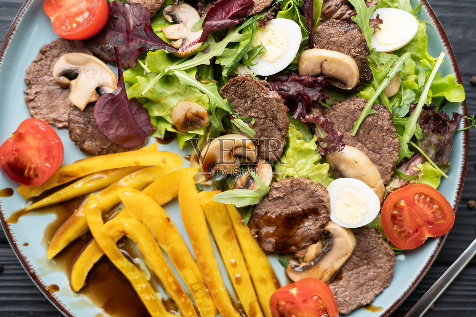 深色木质背景上，俯视平铺的温热沙拉，配有三分熟的牛肉饼和烤蔬菜照片摄影图片
