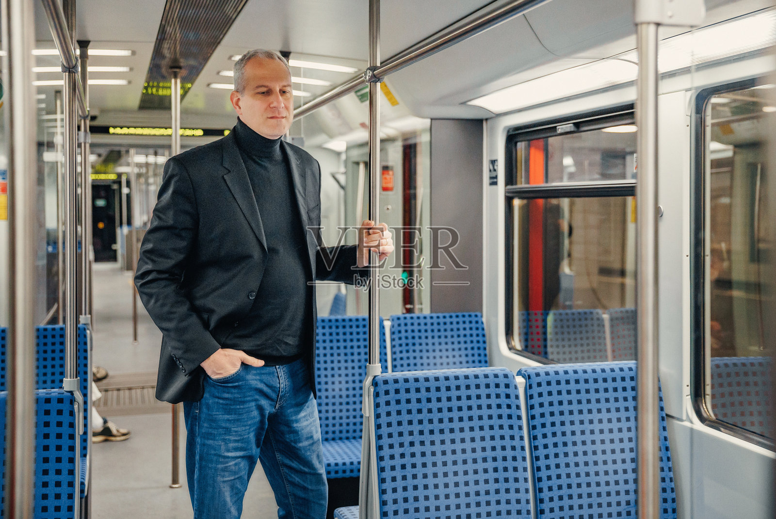 中年男子站立在地铁列车中，手抓扶杆，在上班途中照片摄影图片