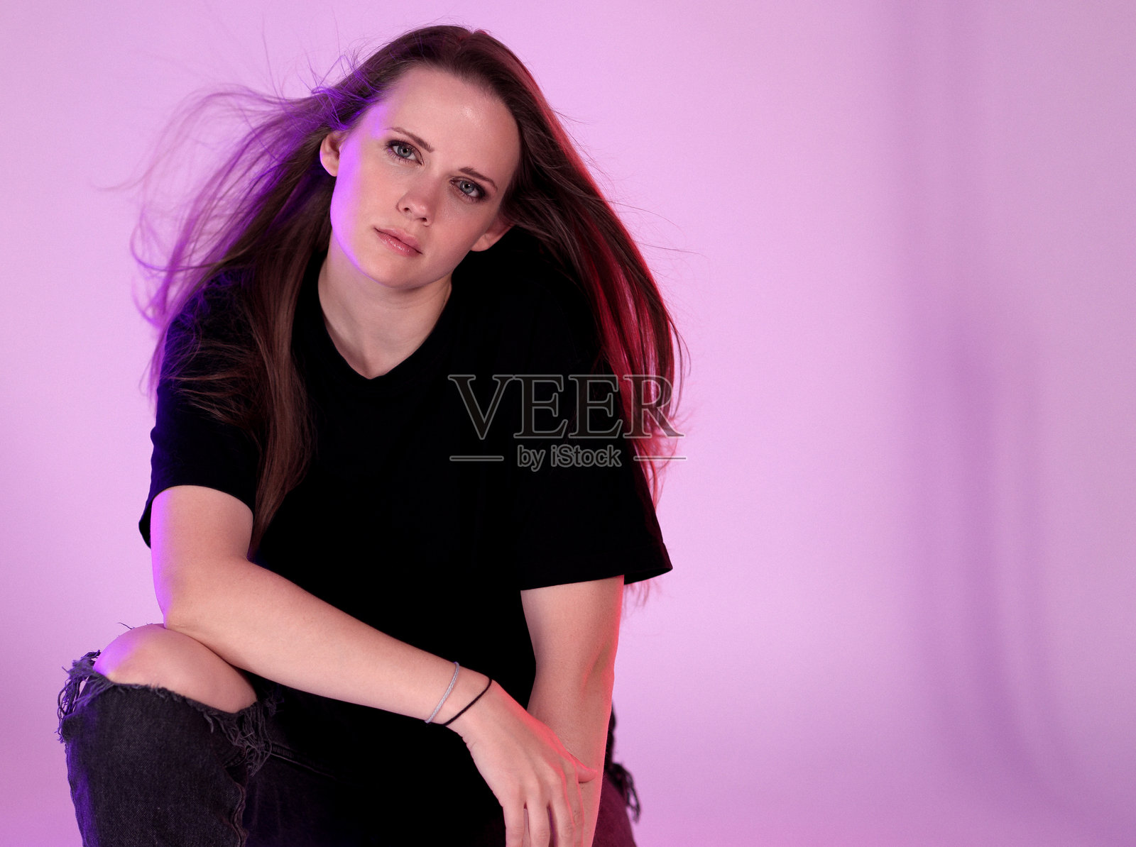 年轻女子在紫色背景前摆姿势，长发在风中飘动照片摄影图片